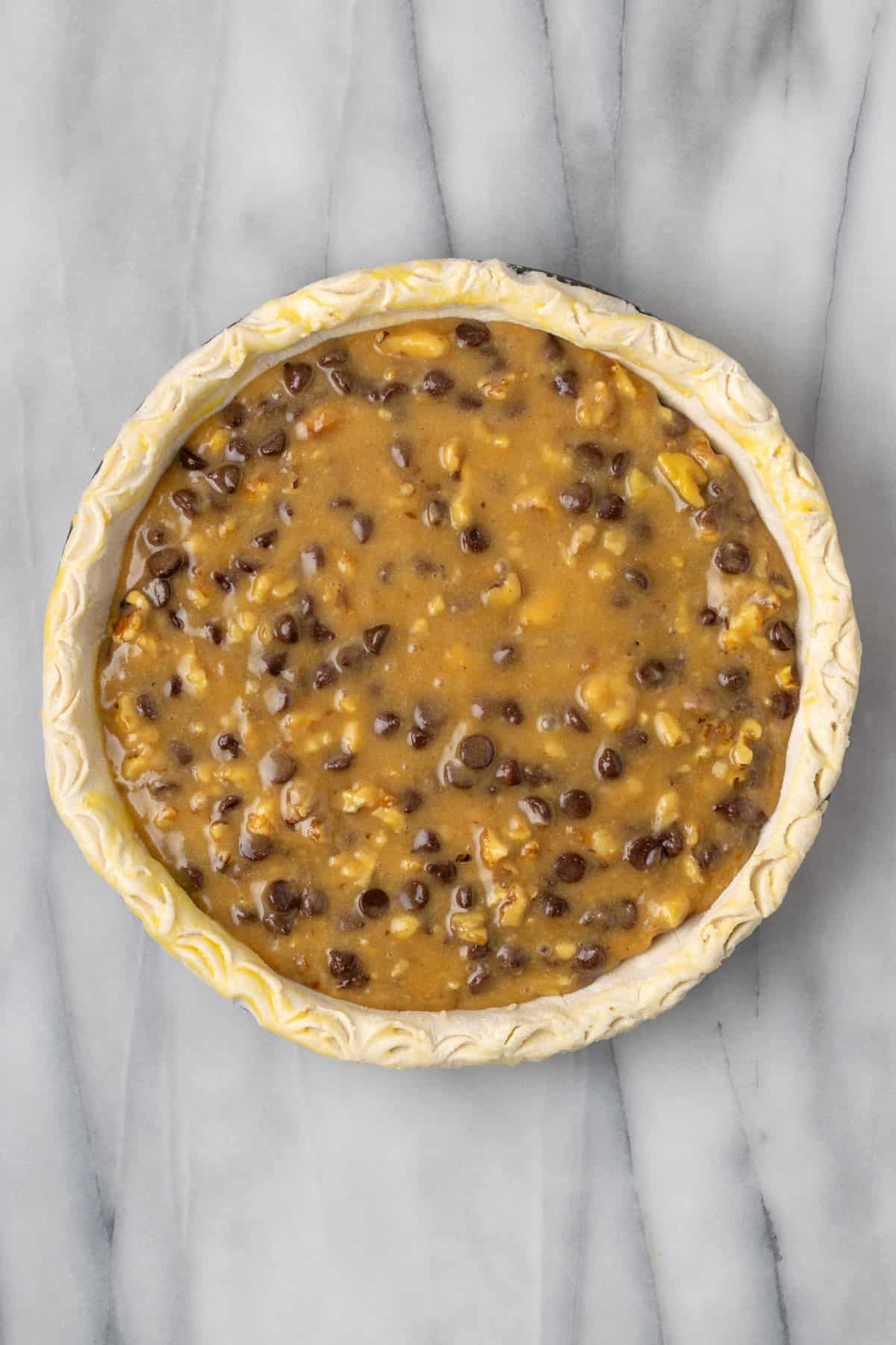 An unbaked Kentucky derby pie sitting on a white marble table.