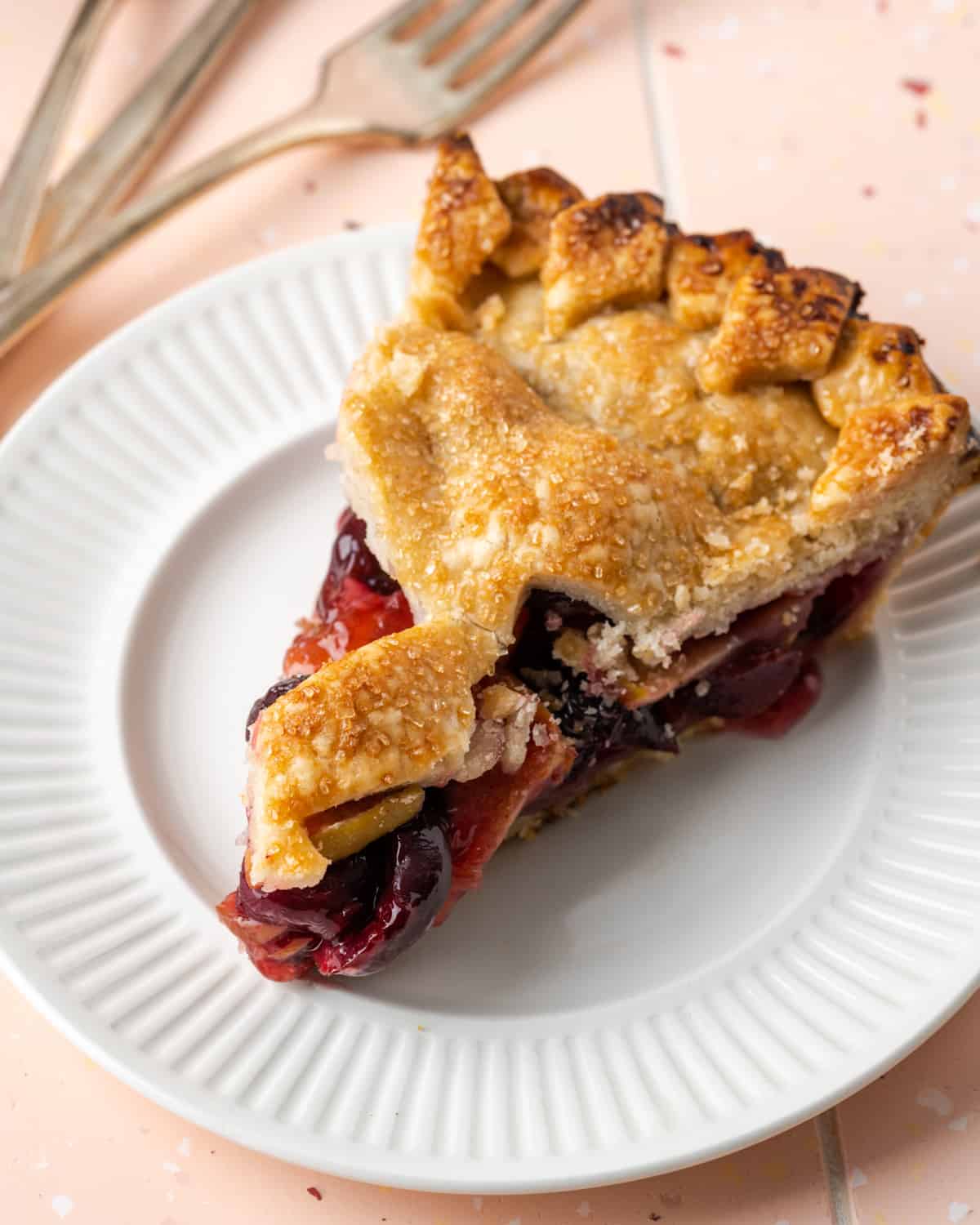 A slice of apple cherry pie on a white plate.