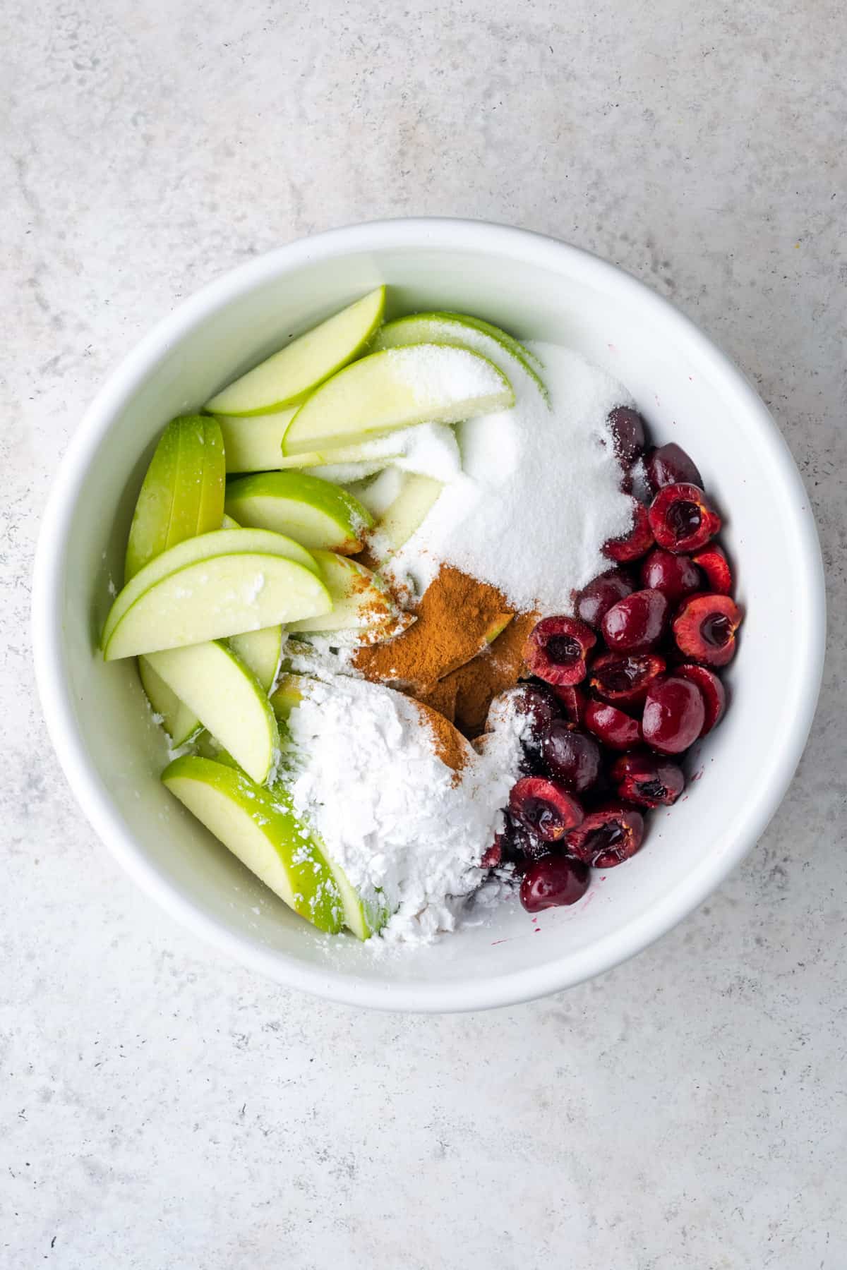 Apple cherry pie ingredients combined together in a large white mixing bowl.