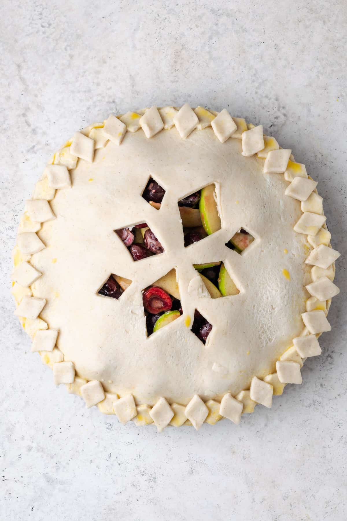 An unbaked pie with a decorative crust made of diamond shapes cut out and placed around the edge of the crust.