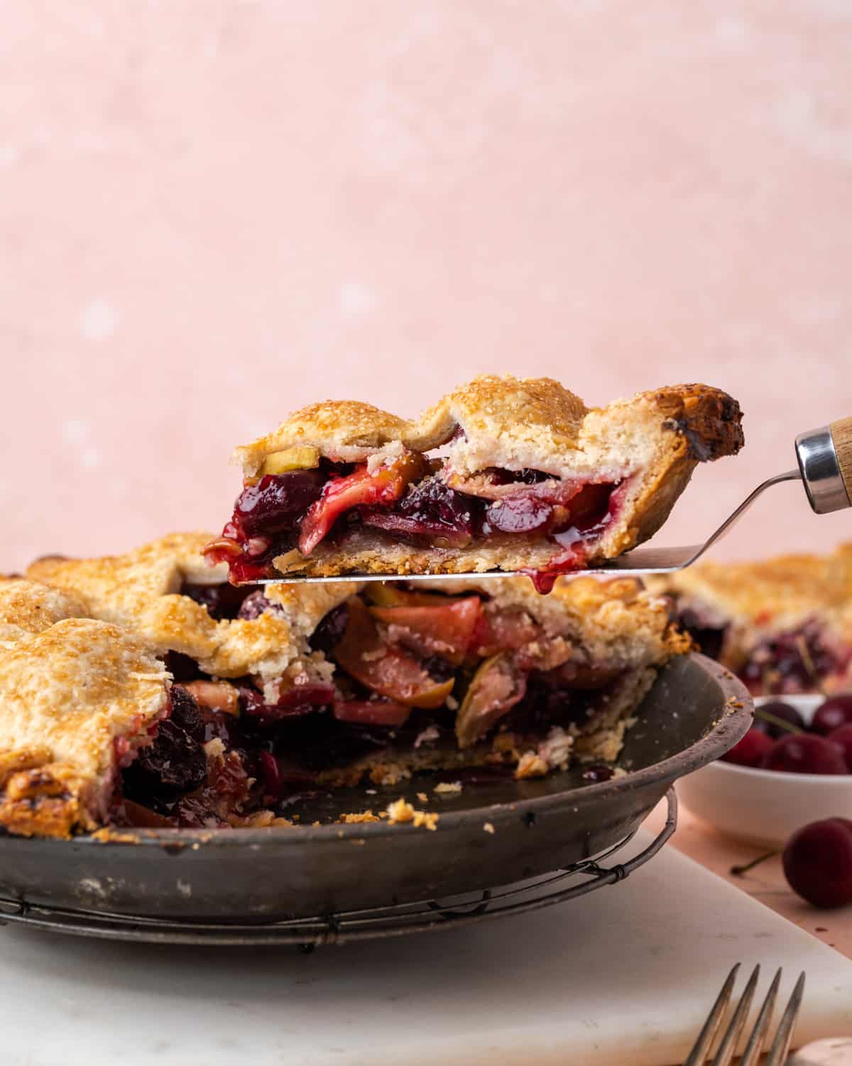 A slice of apple cherry pie being lifted from a pie plate.