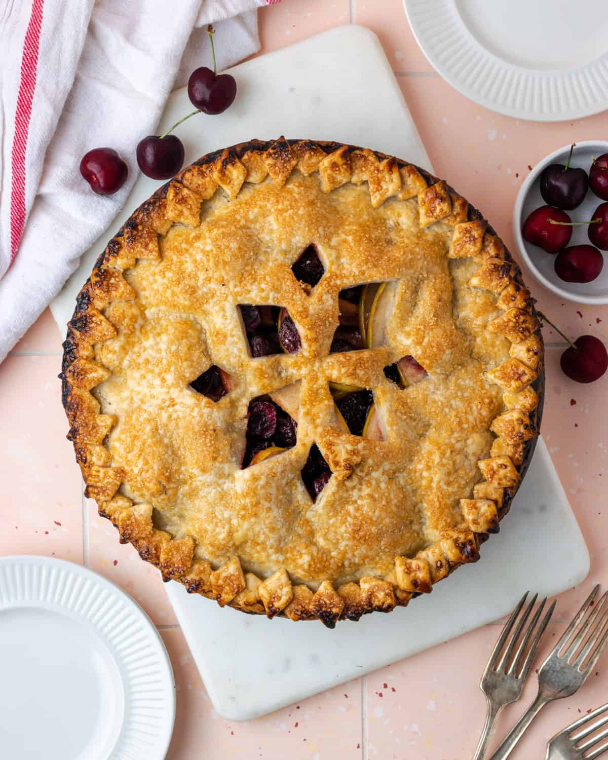 A freshly baked apple cherry pie on a white cutting board.