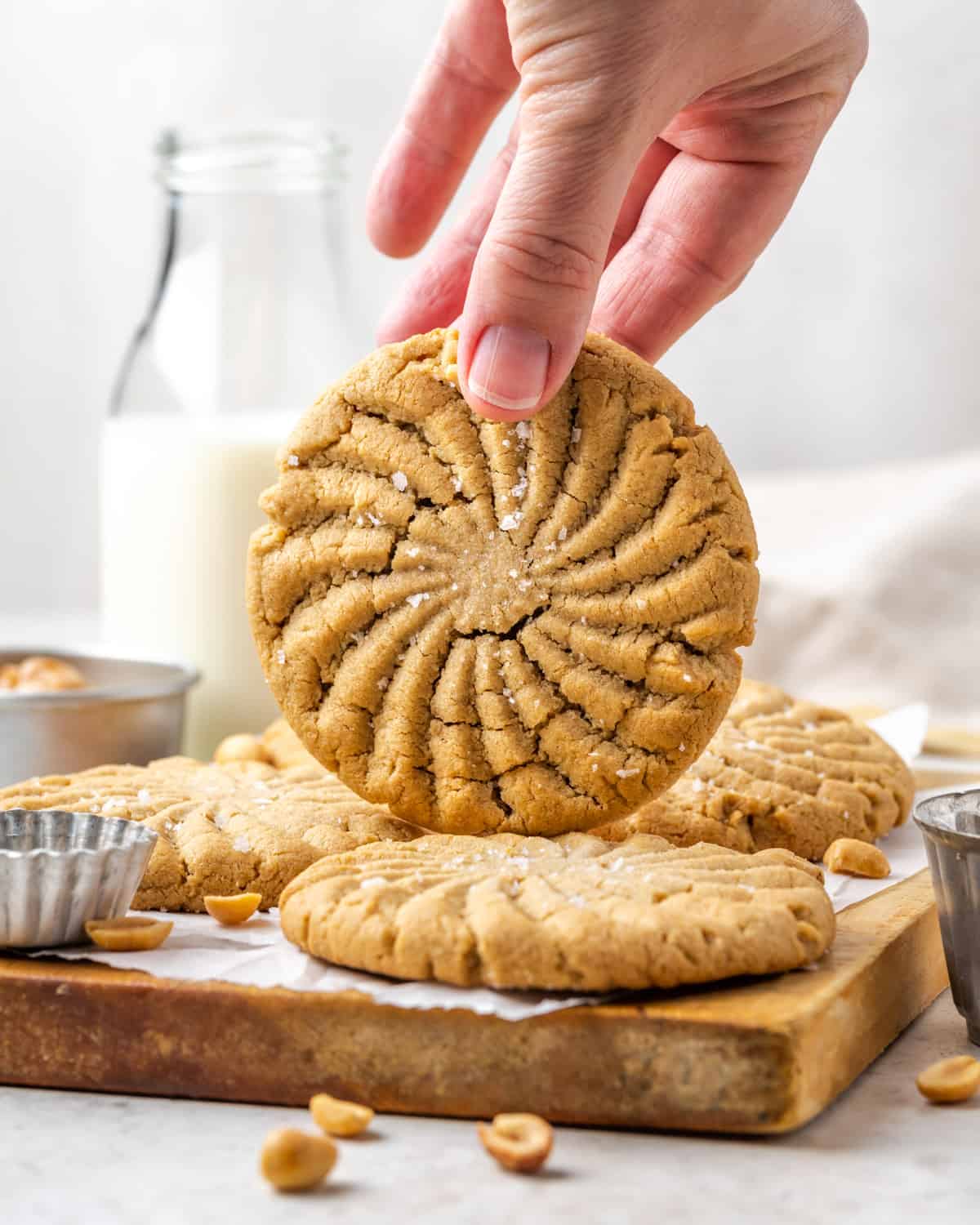 A hand picking up a large peanut butter cookie from a cutting board.