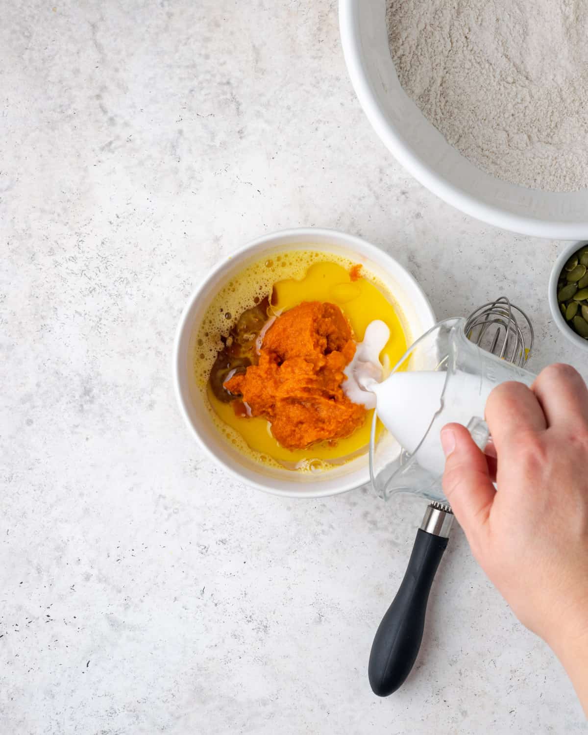 Oil, vanilla, pumpkin puree and milk being added to the beaten egg. 