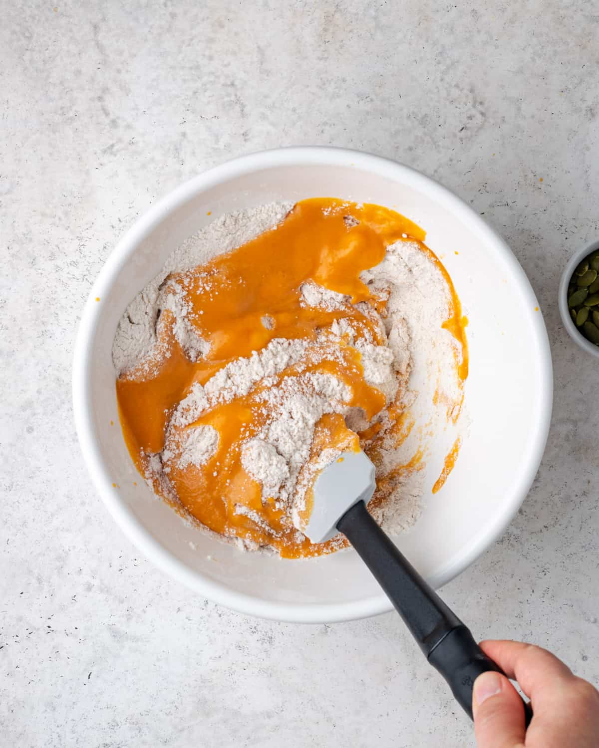 Wet ingredients being folded into dry ingredients in a large white mixing bowl.