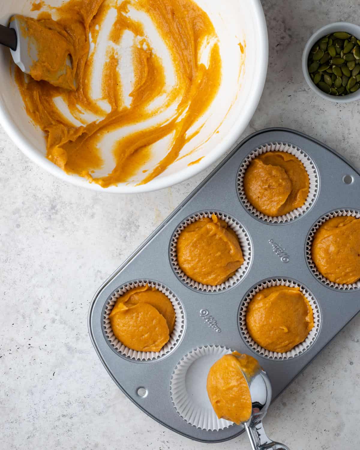 Pumpkin muffin batter being portioned into a muffin tin with an ice cream scoop.