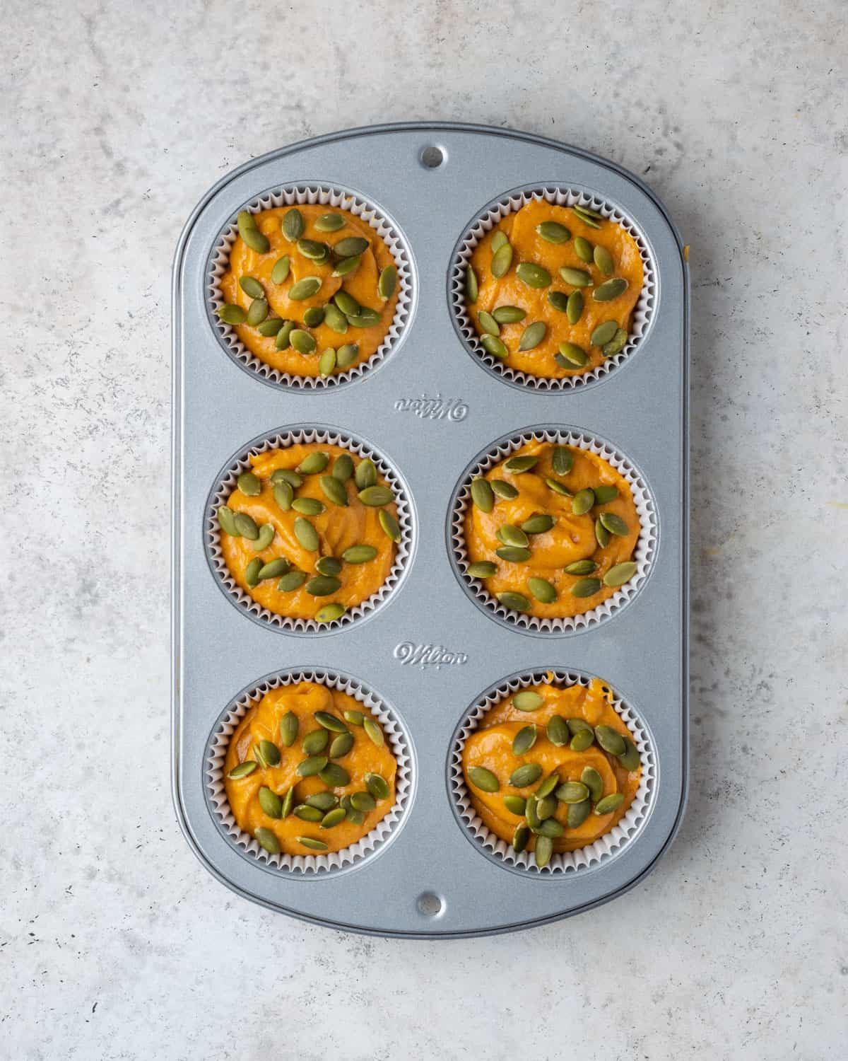 Unbaked gluten free pumpkin muffin batter topped with pumpkin seeds.