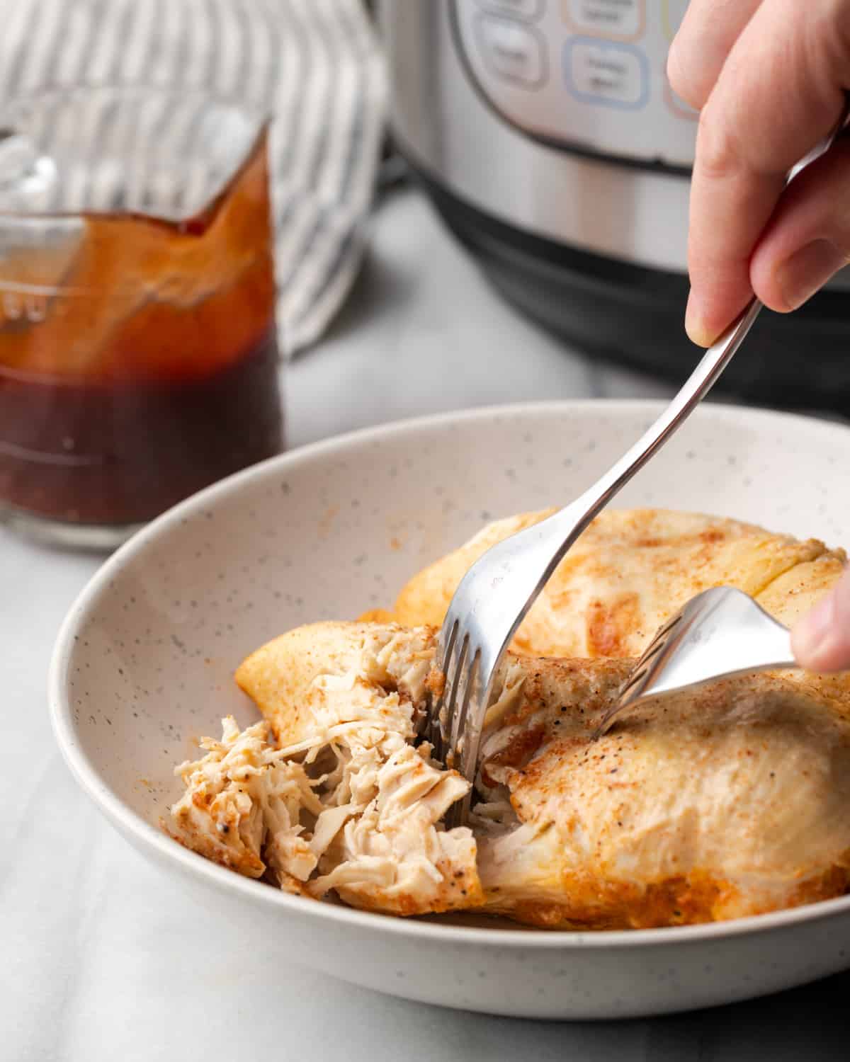 Two cooked chicken breasts being pulled with a fork. 