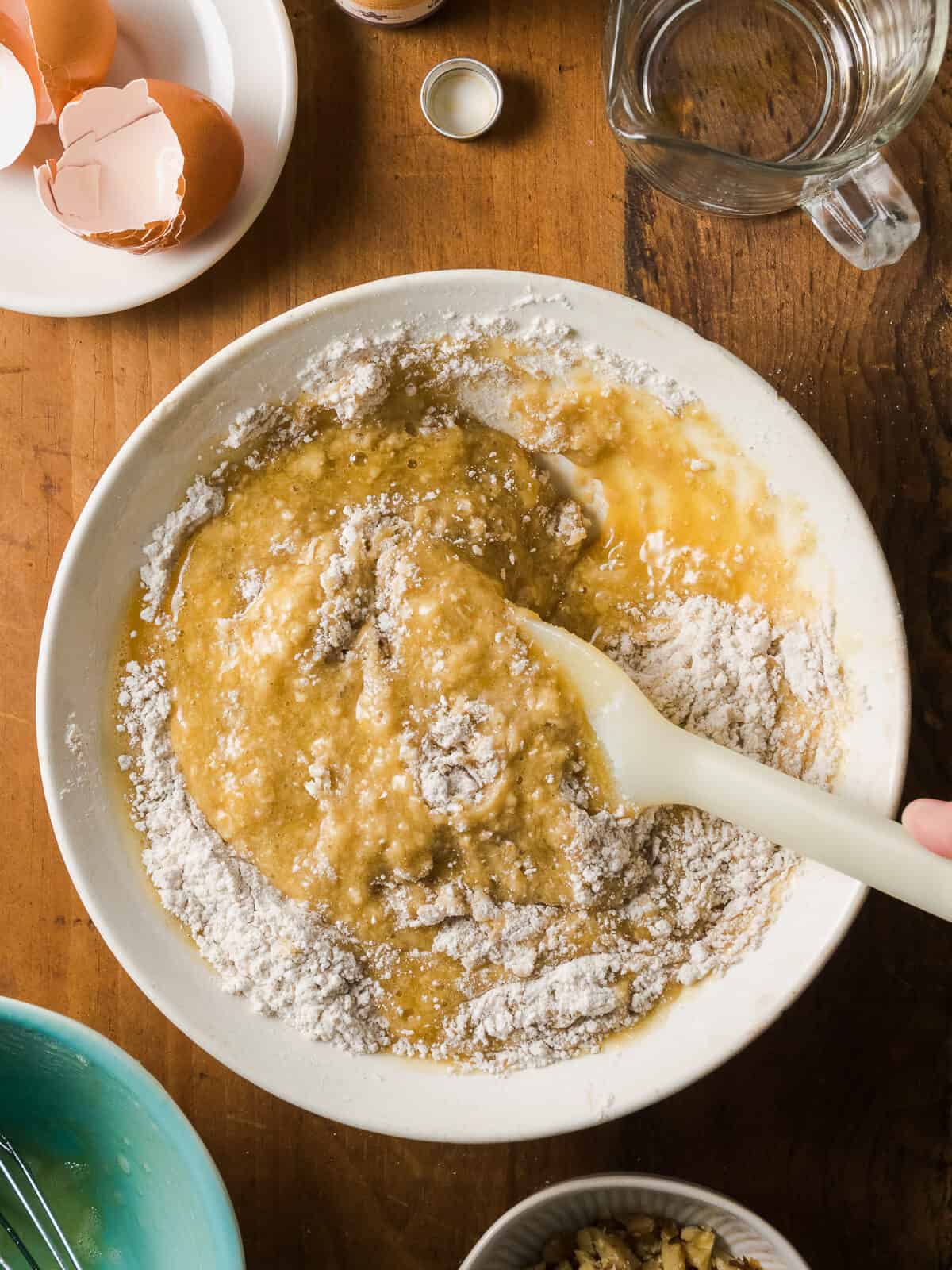 Wet ingredients being folded into dry ingredients with a spatula.