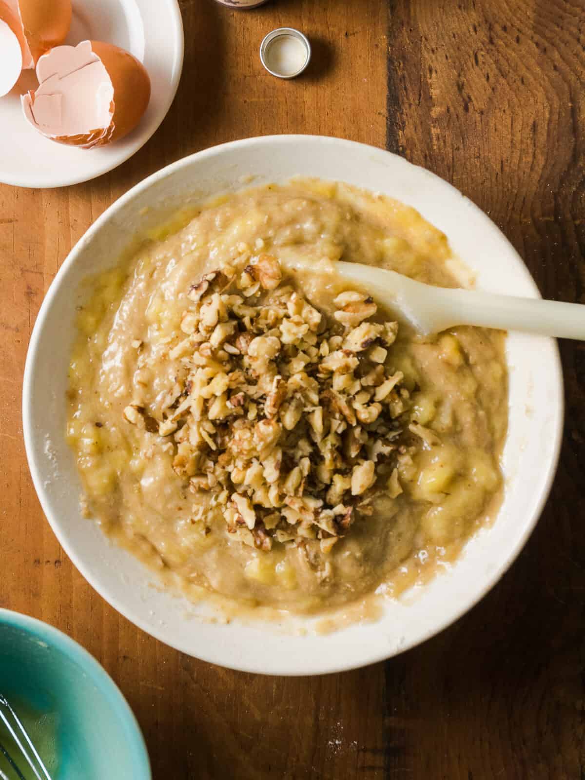 Mashed banana and walnuts being stirred into banana bread batter.