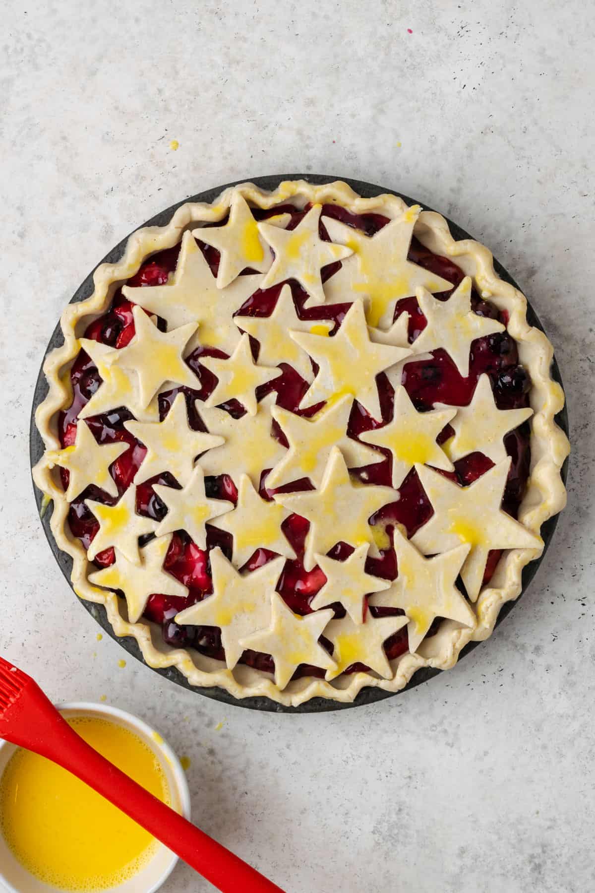 An unbaked strawberry blueberry pie topped with star shapes and brushed with egg wash.