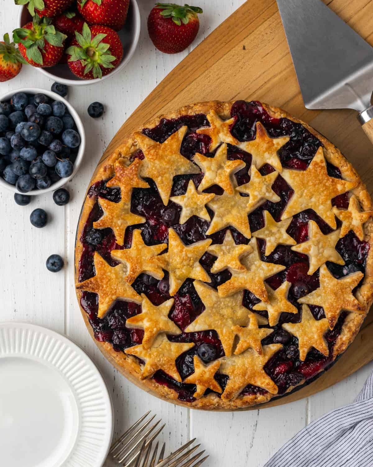 A strawberry blueberry pie topped with star shaped pie crust on a white table.