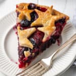 A slice of strawberry blueberry pie topped with star shaped pie crust on a white plate.