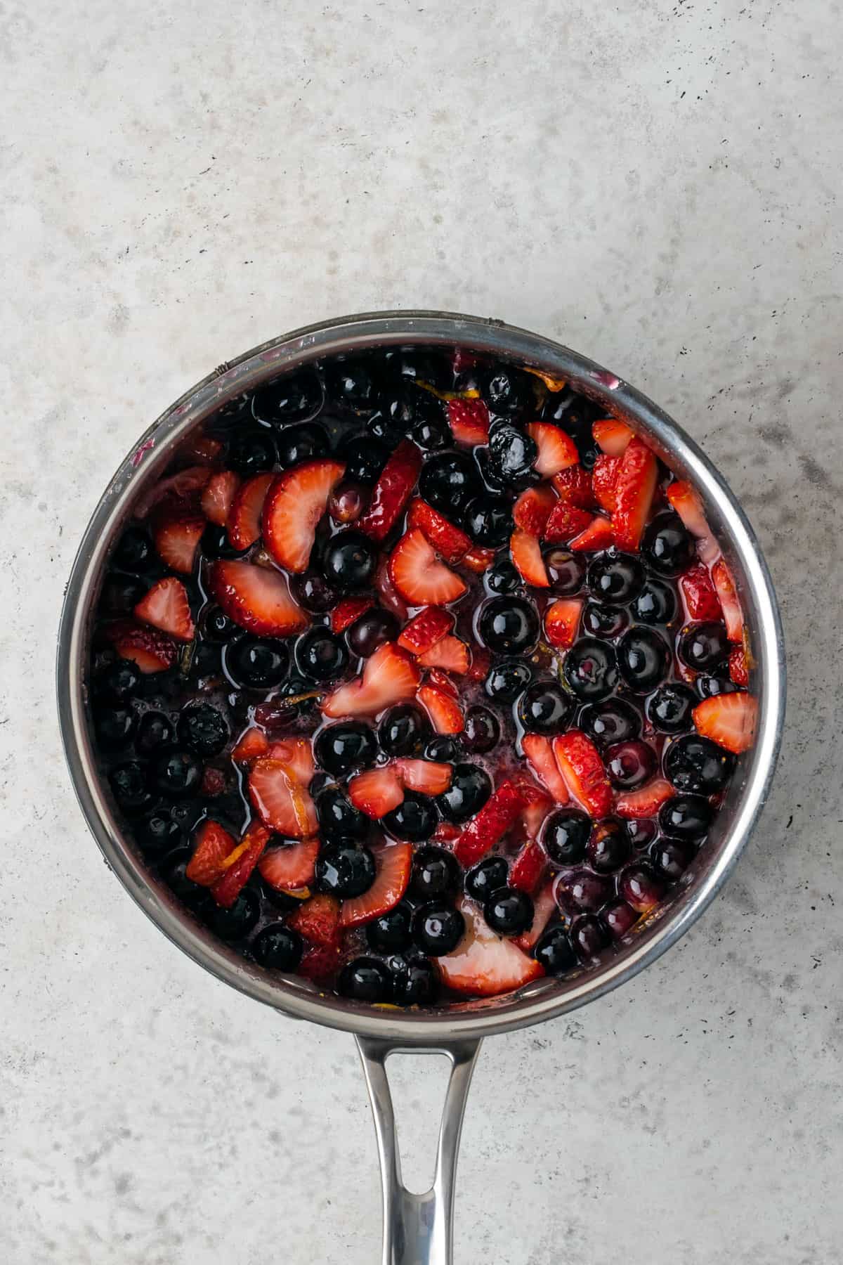 Partially cooked strawberries and blueberries in a saucepan.