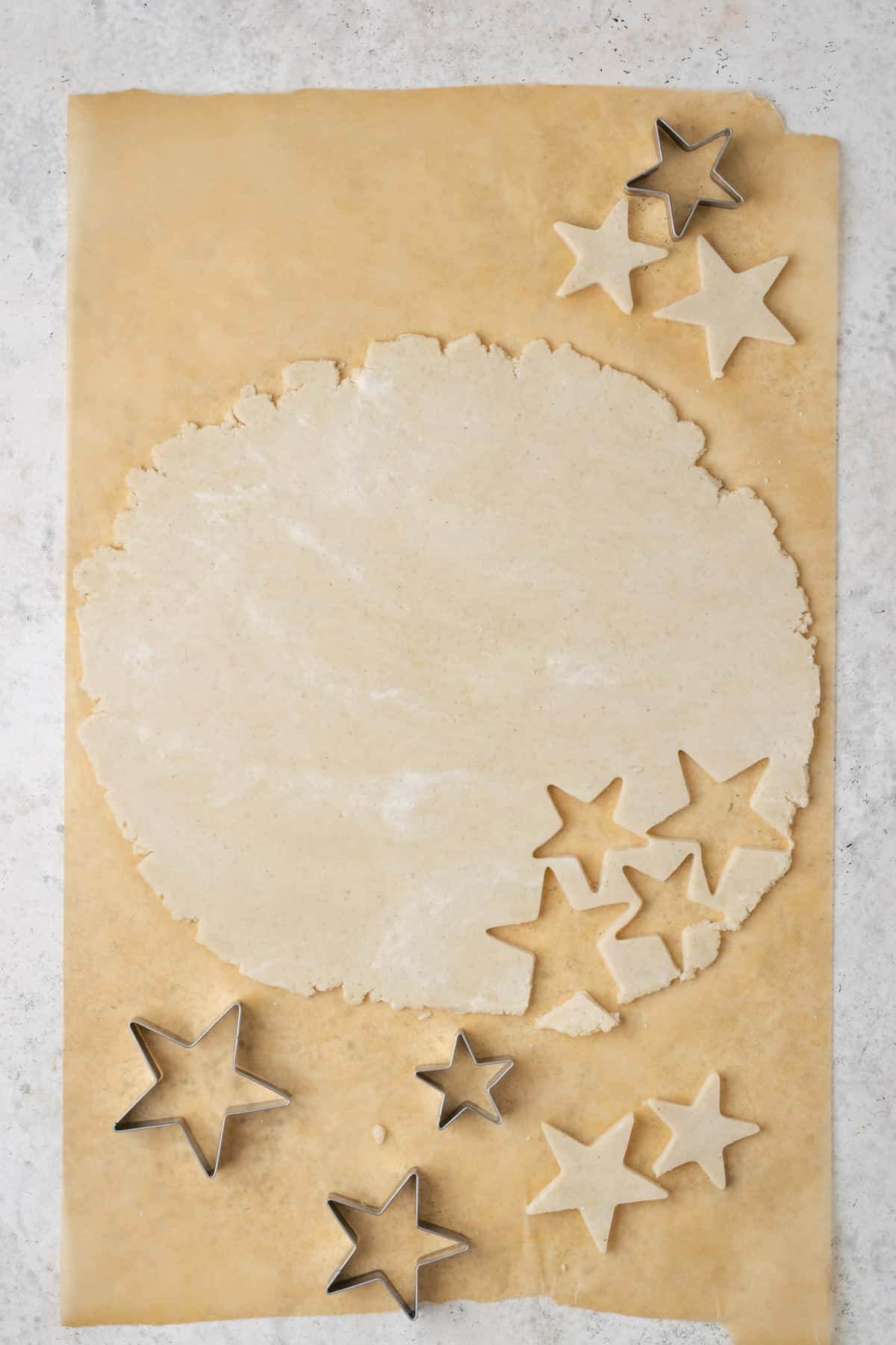 A sheet of pie dough rolled out and star shaped cookie cutters on a white table.