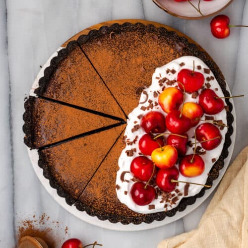 A sliced chocolate ganache tart topped with whipped cream and fresh cherries.