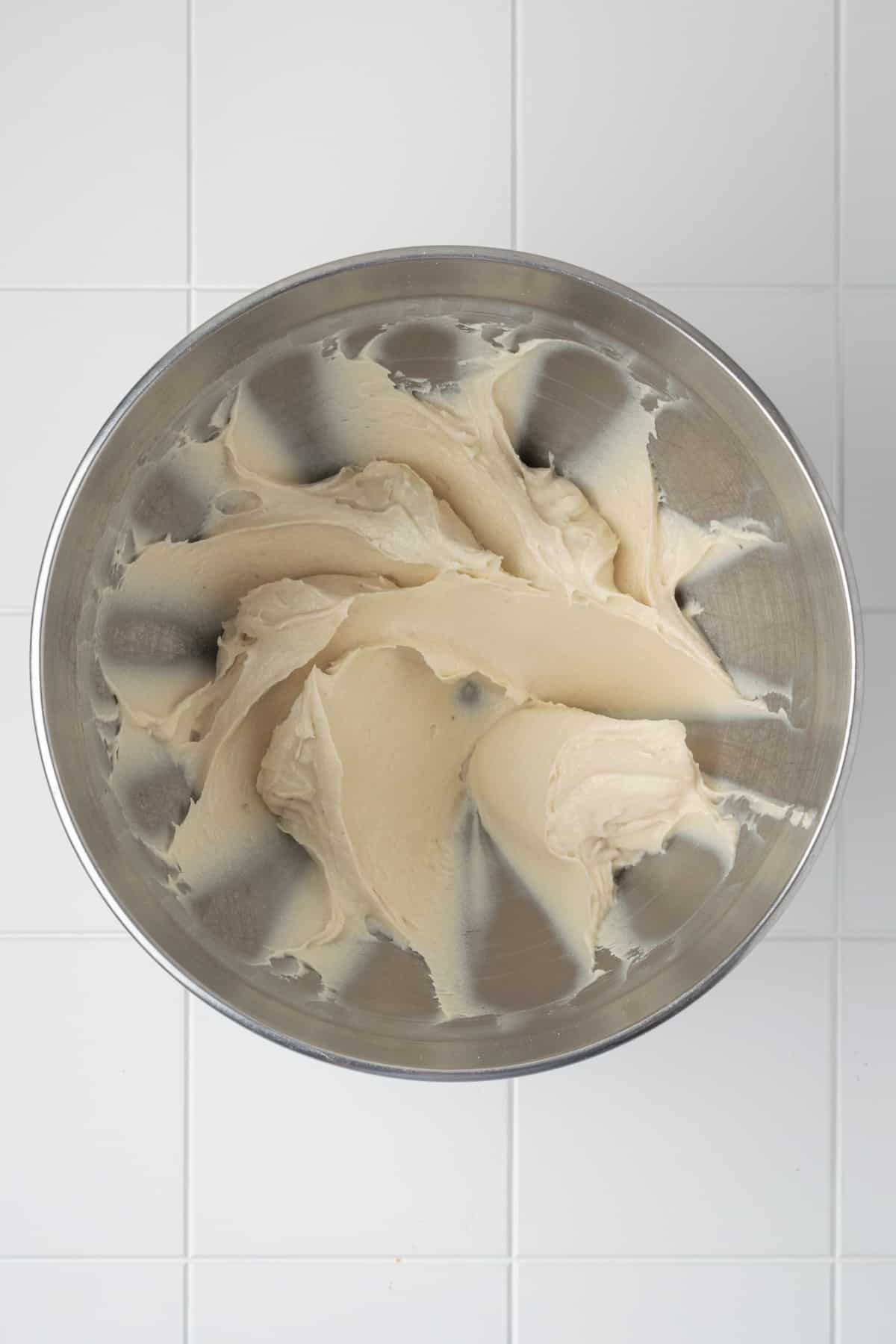 Vegan cream cheese, vegan sour cream, powdered sugar, vanilla, and lemon juice beaten together in a metal mixing bowl.