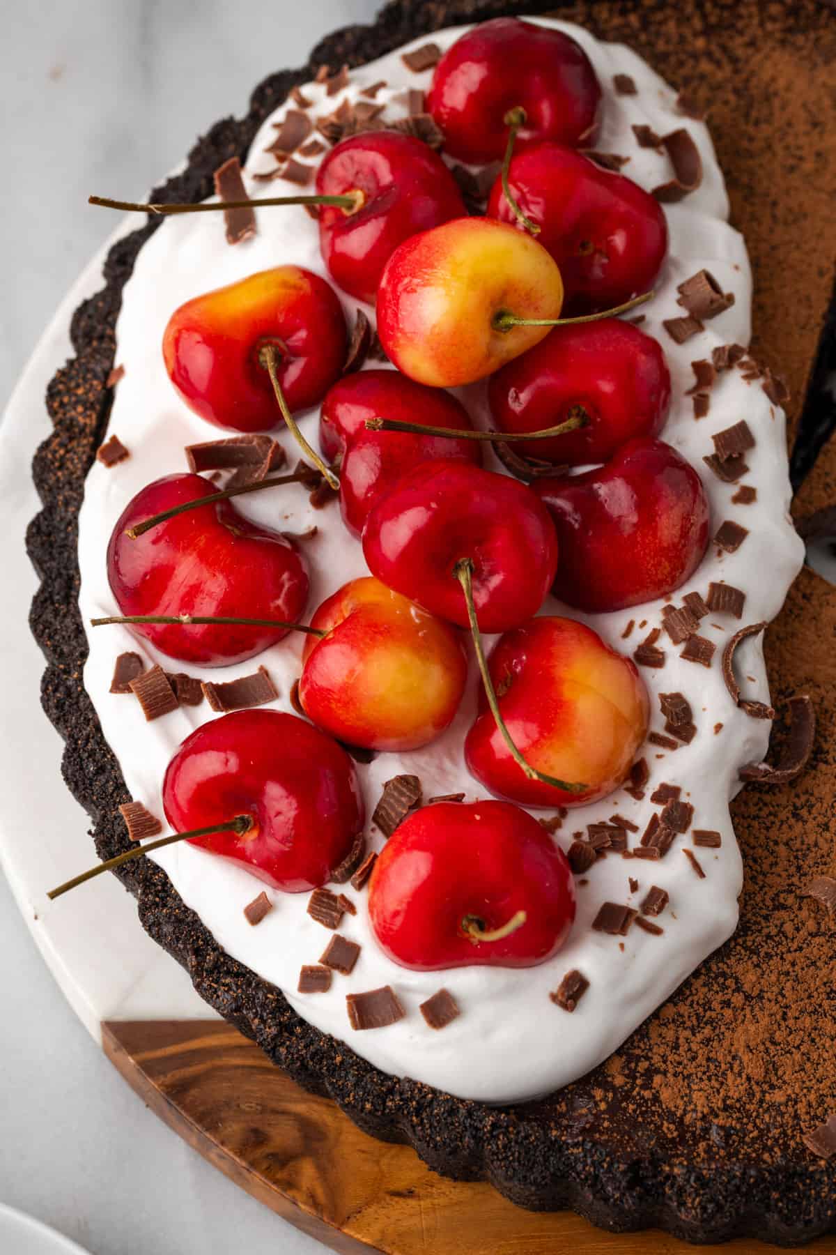 A dark chocolate tart covered with whipped cream and fresh cherries.
