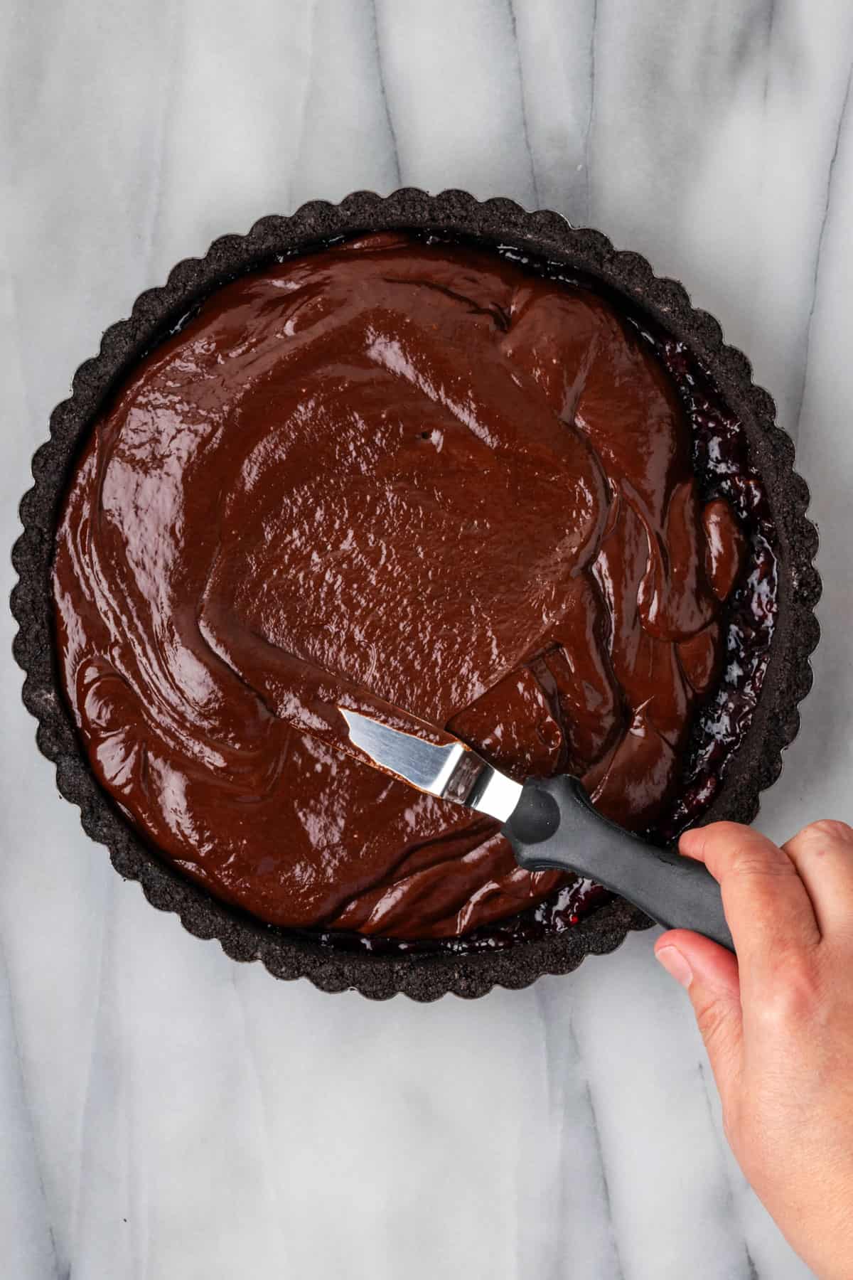Chocolate ganache being spread over the cherry filling with an offset spatula.