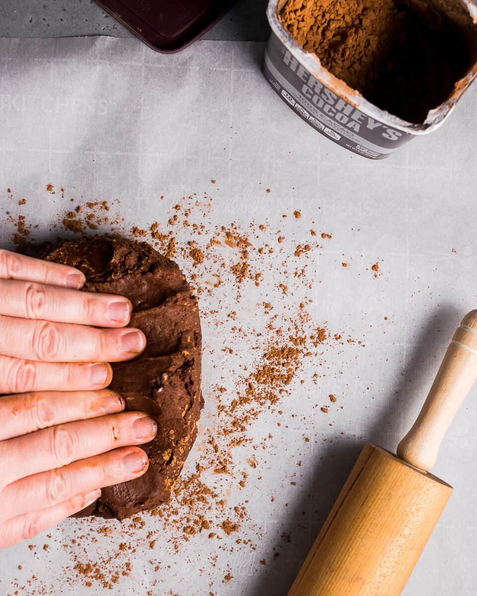 Hands kneading chocolate cookie dough on a piece of parchment paper.