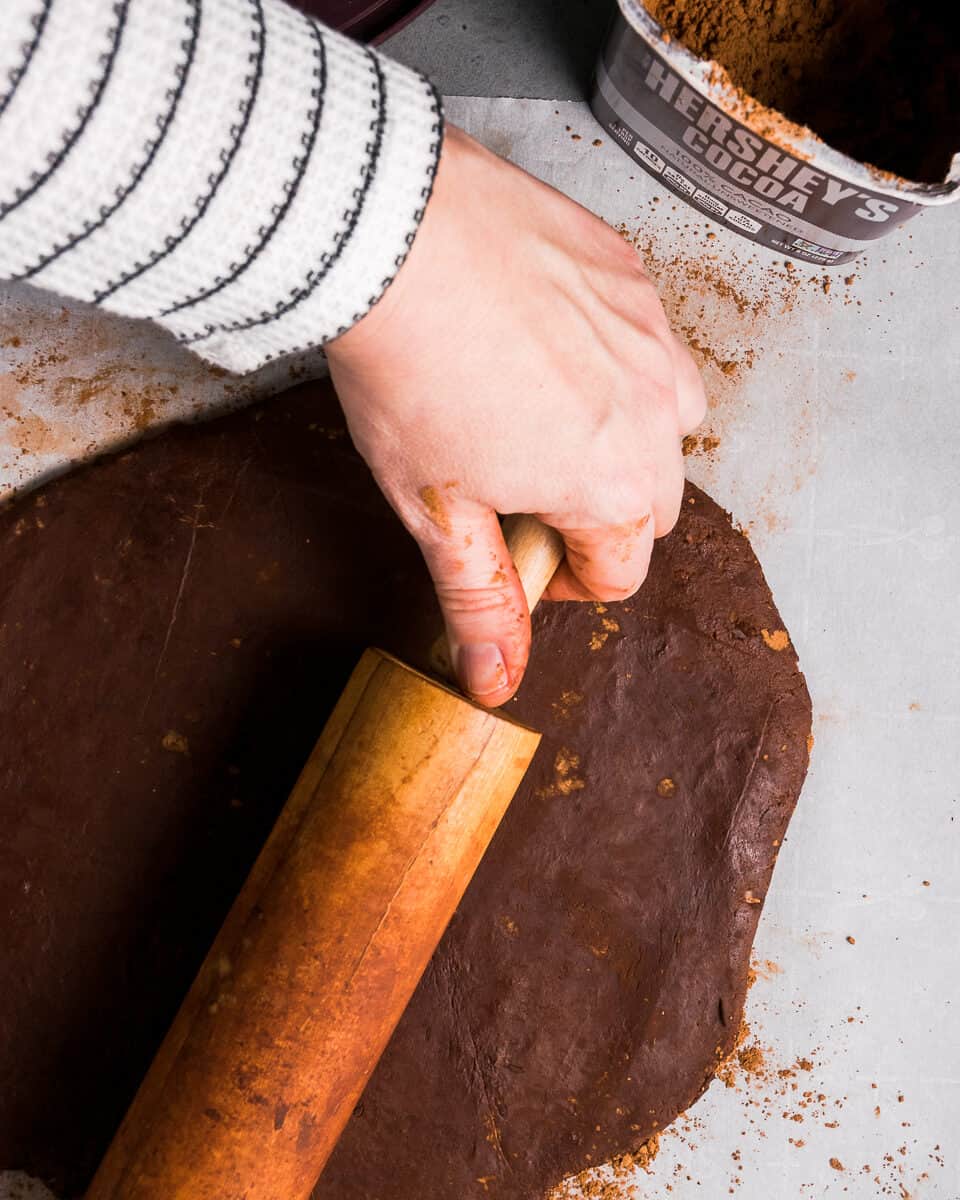 A rolling pin being used to roll out thin mint cookie dough into a sheet.