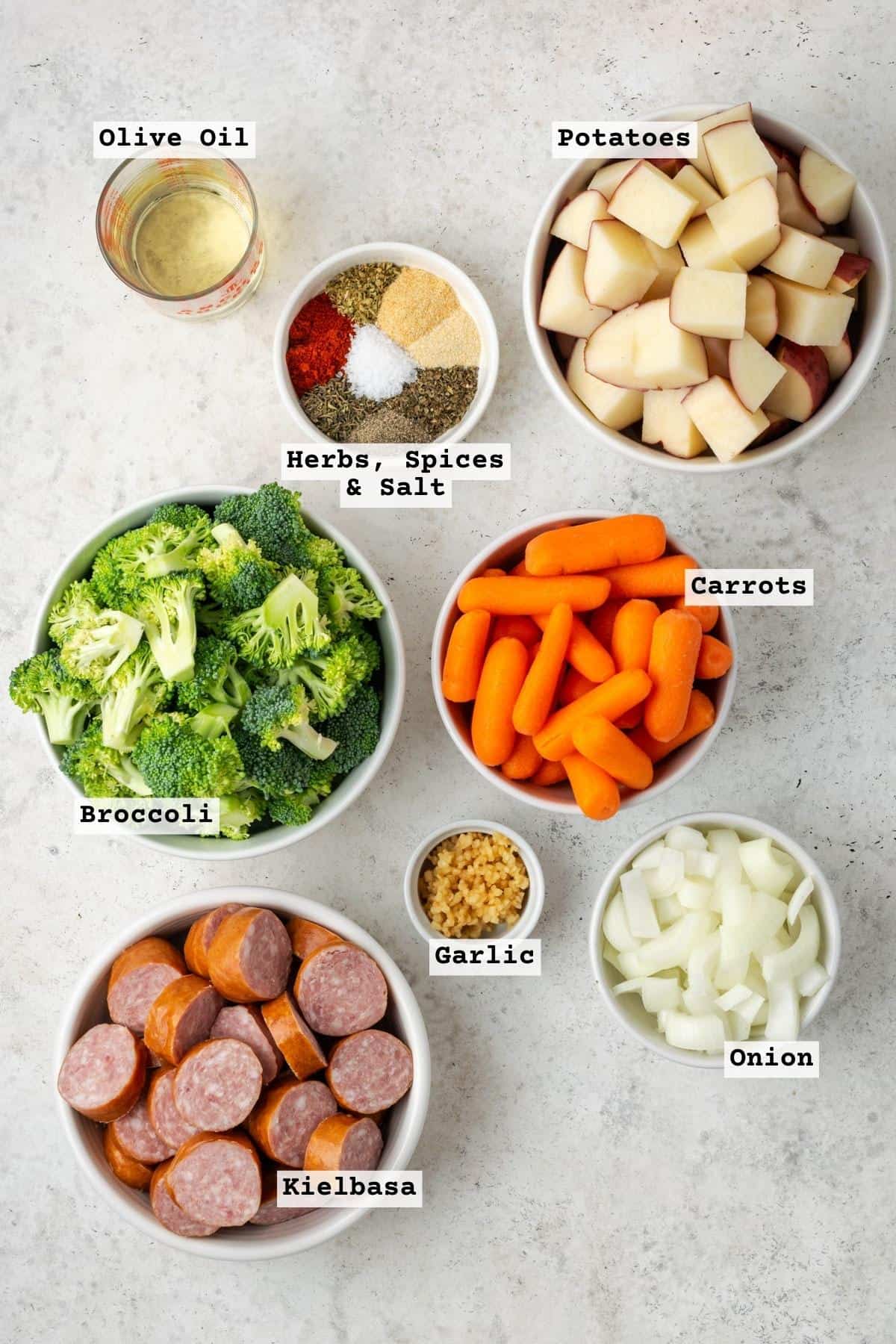 Ingredients for sausage and veggies sheet pan meal on a white table. 