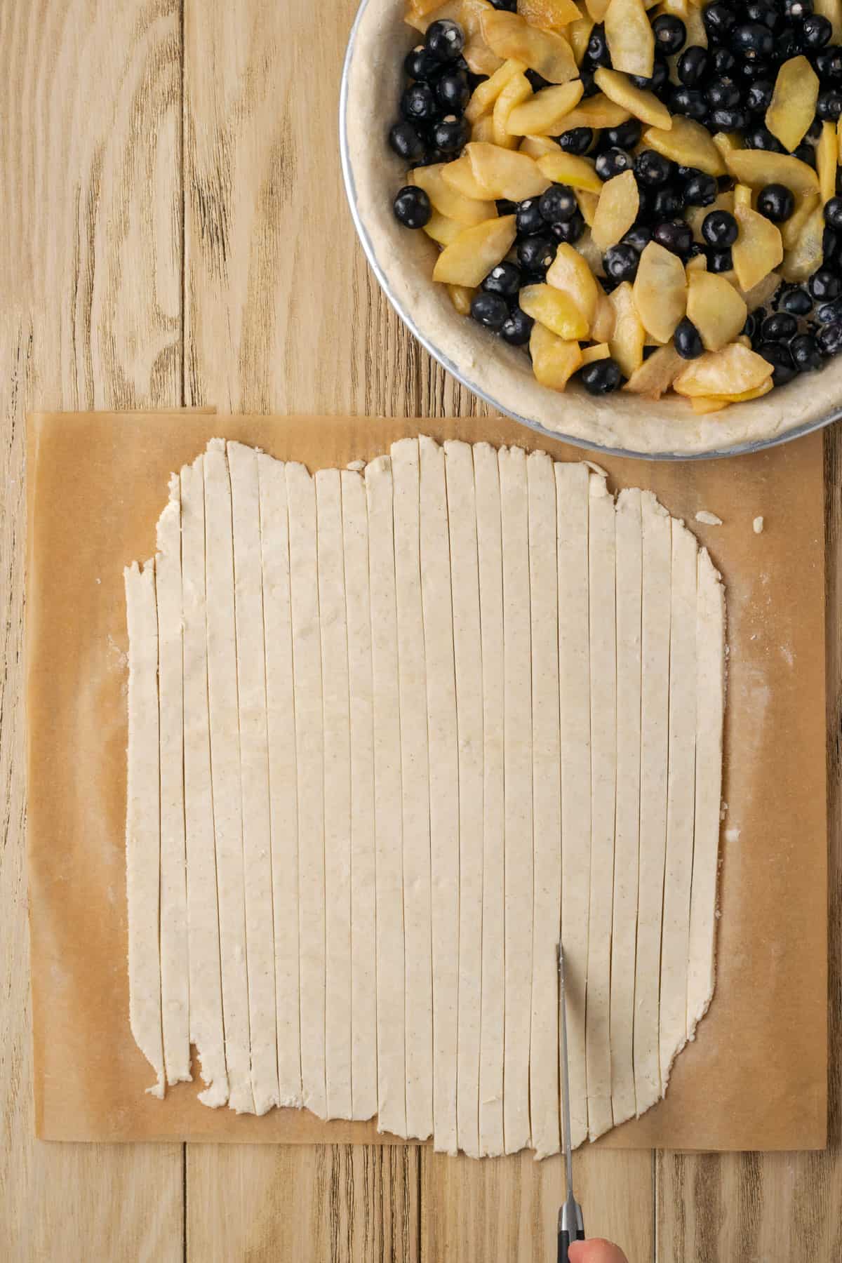 A sheet of pie dough being sliced into thin strips. 