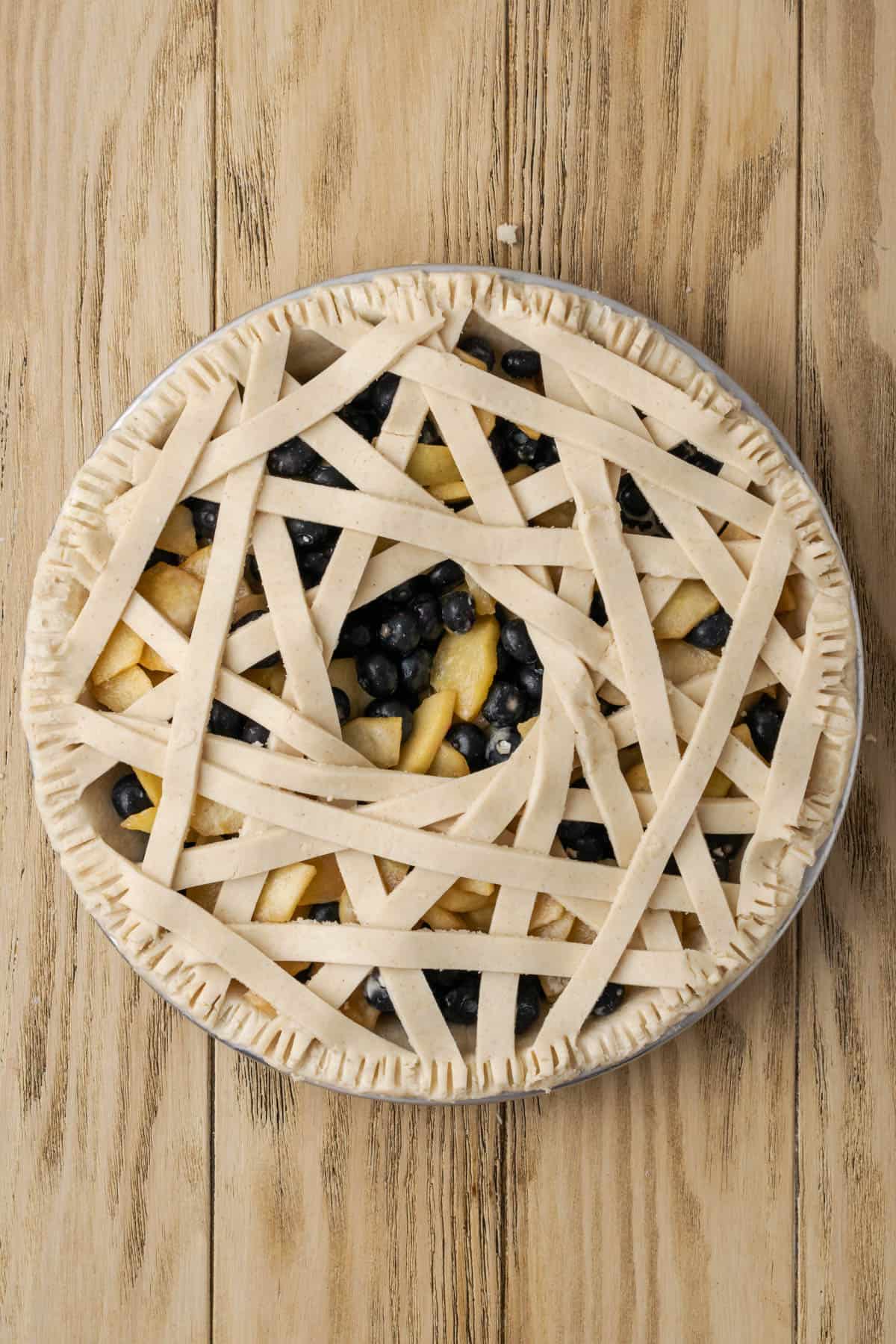 An unbaked apple blueberry pie with a decorative lattice top sitting on a wooden table. 