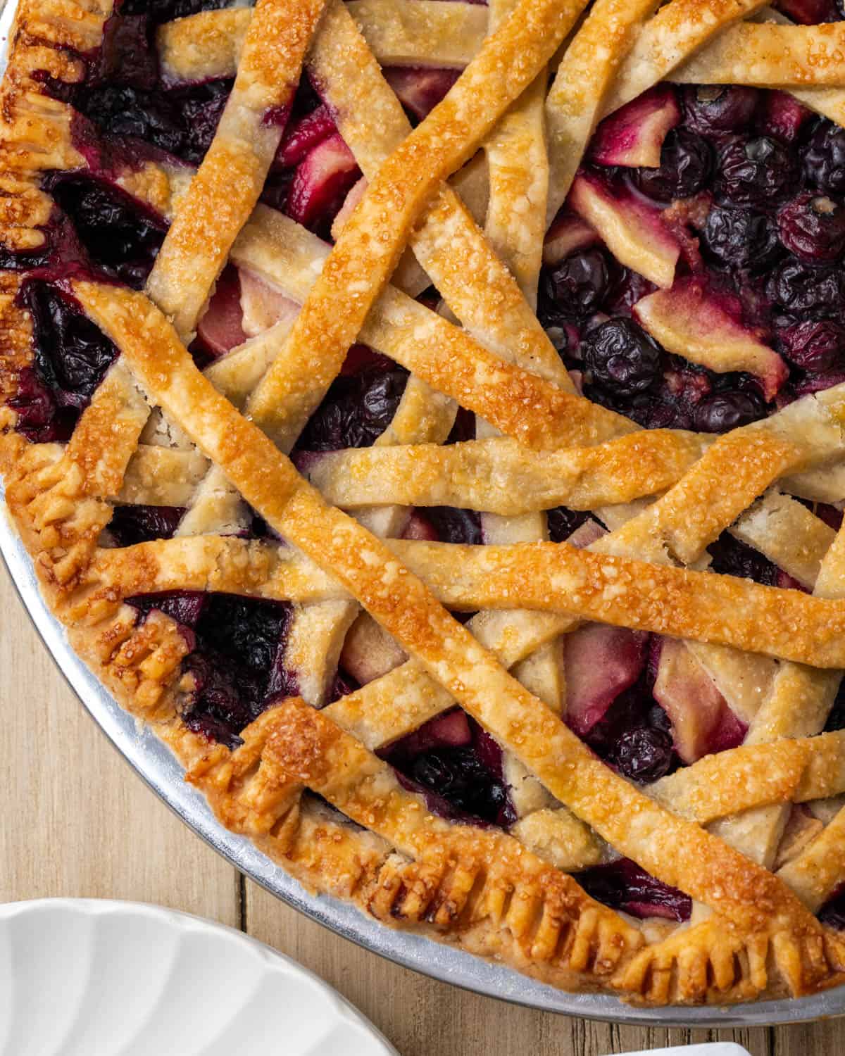 A freshly baked apple blueberry pie sitting on a wooden table. 