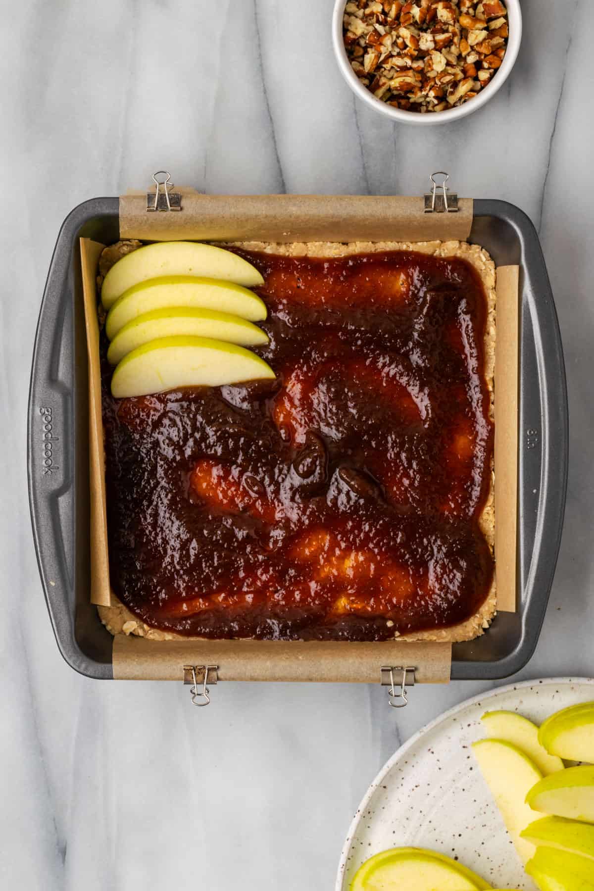 Apple slices placed over the layer of apple butter in a square baking tin.