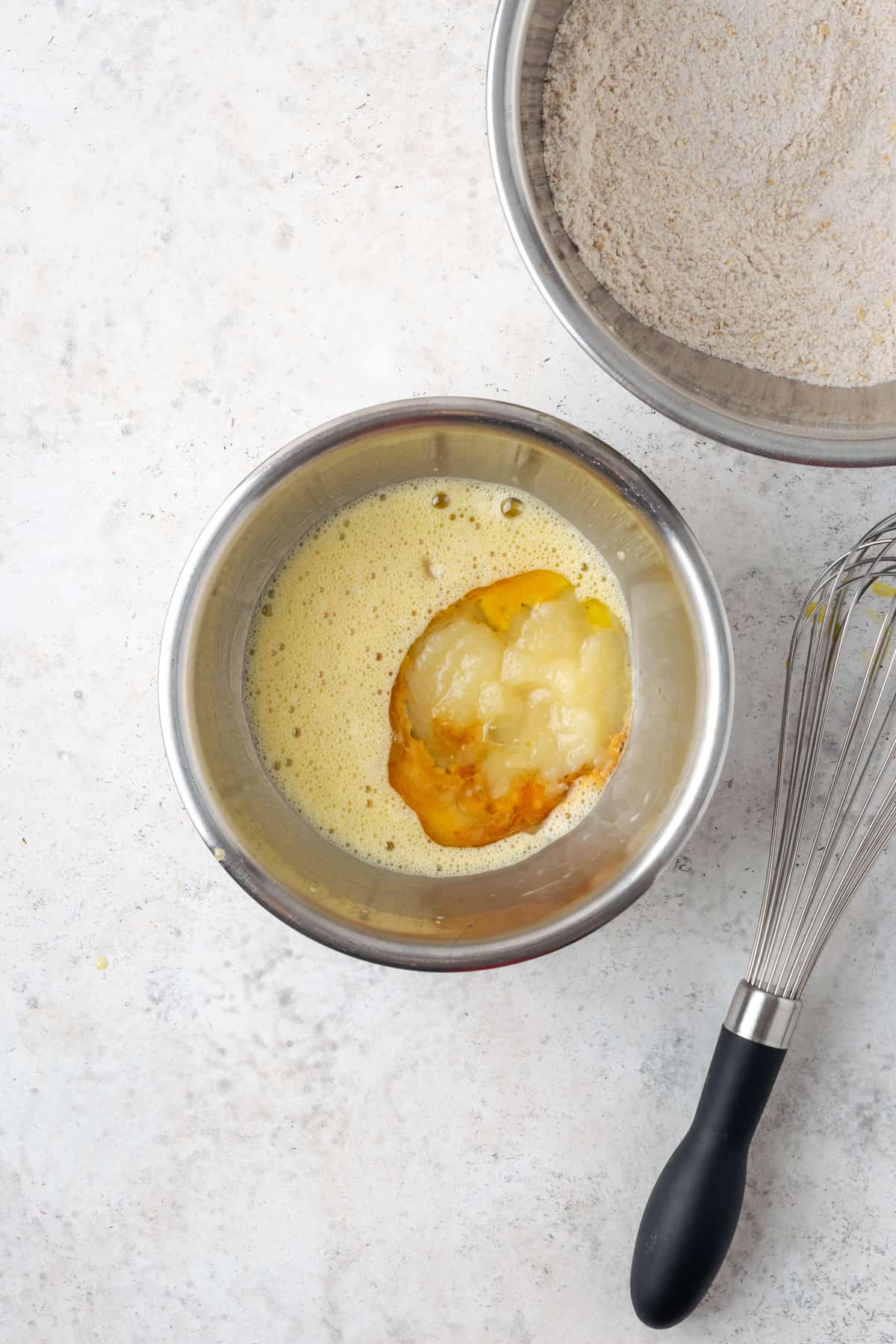 Oil, vanilla, milk, maple syrup and applesauce added to a small mixing bowl containing a beaten egg.