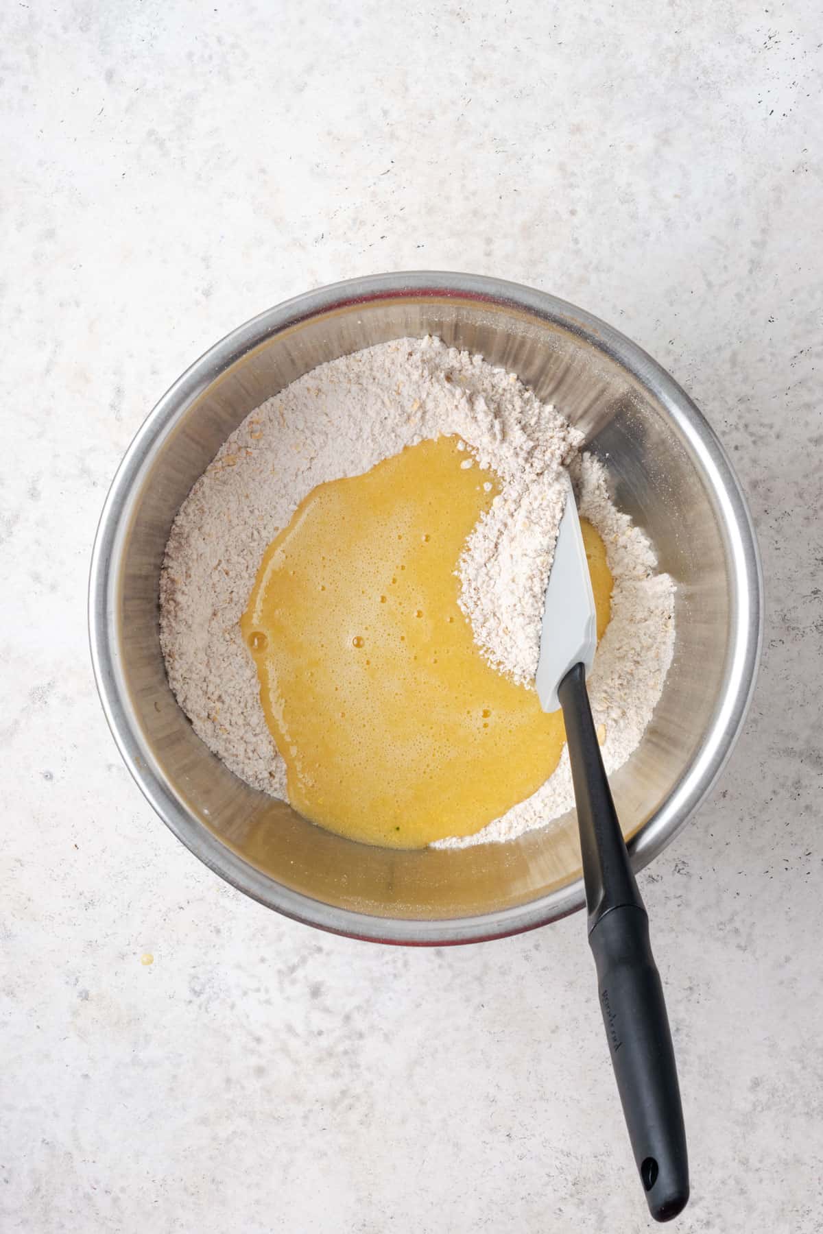 Wet ingredients poured into the dry ingredients into a large metal mixing bowl.