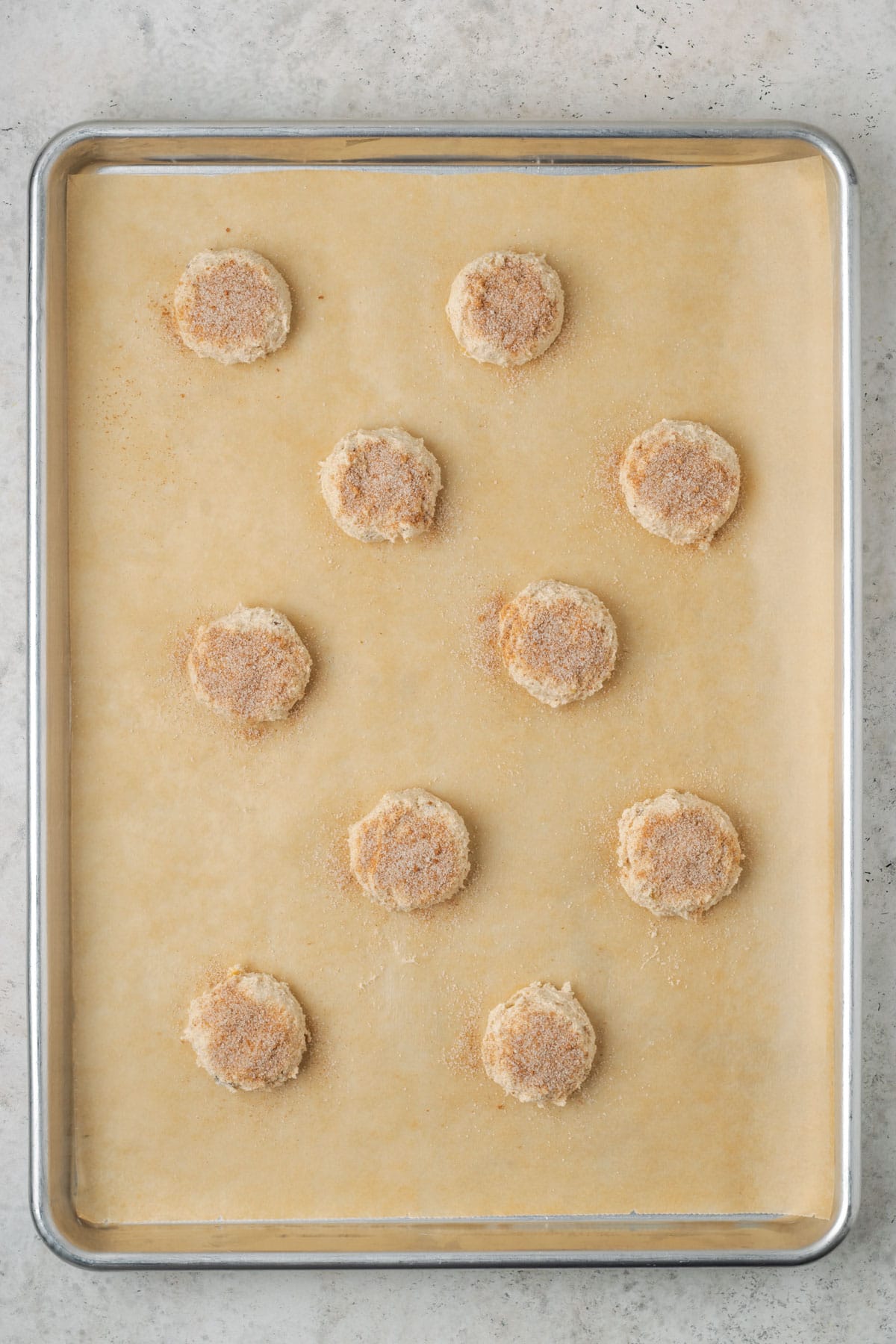 Cinnamon sugar cookie dough balls sprinkled with cinnamon spread out on a baking sheet.