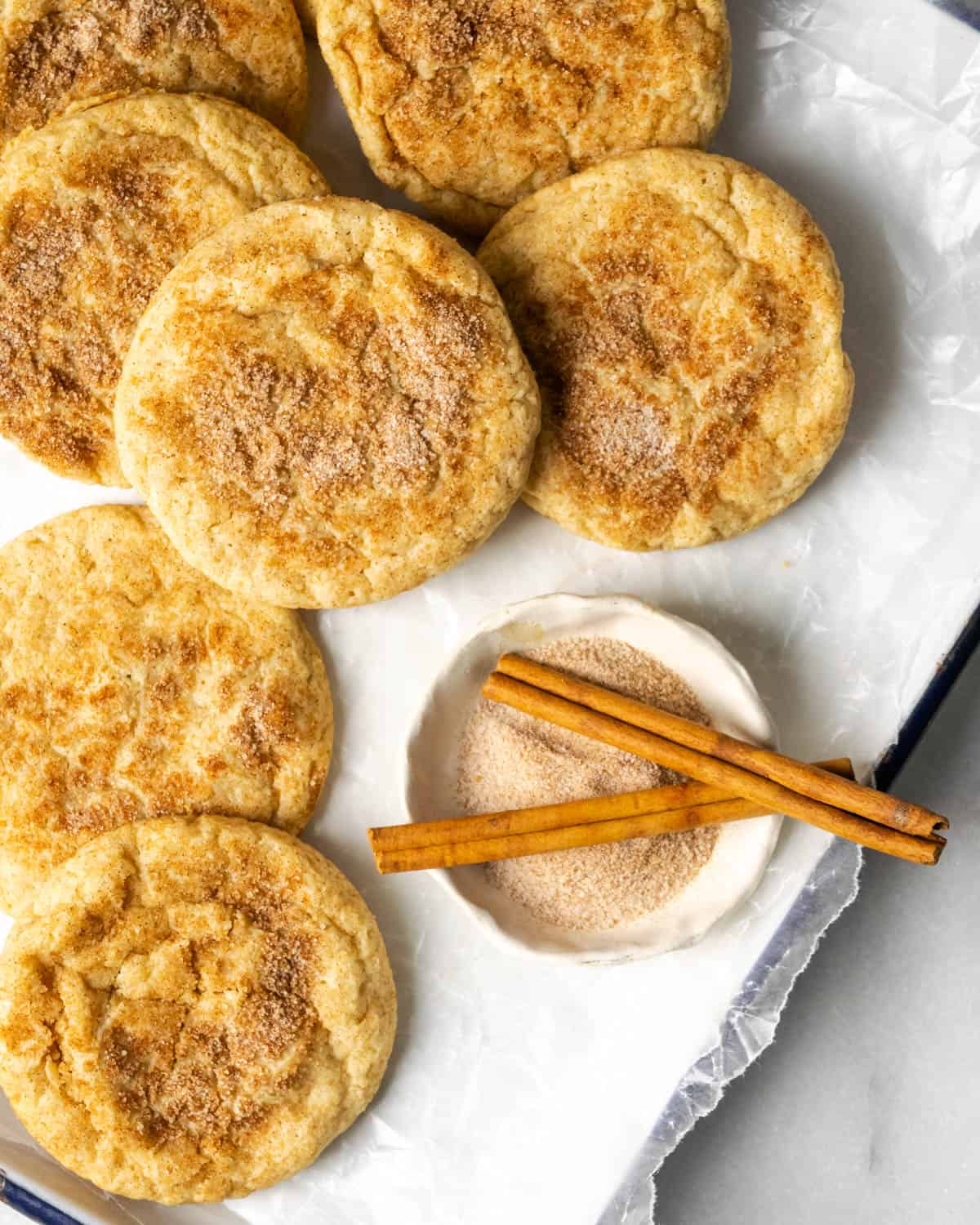 Cinnamon sugar cookies scattered on a white baking tray. 