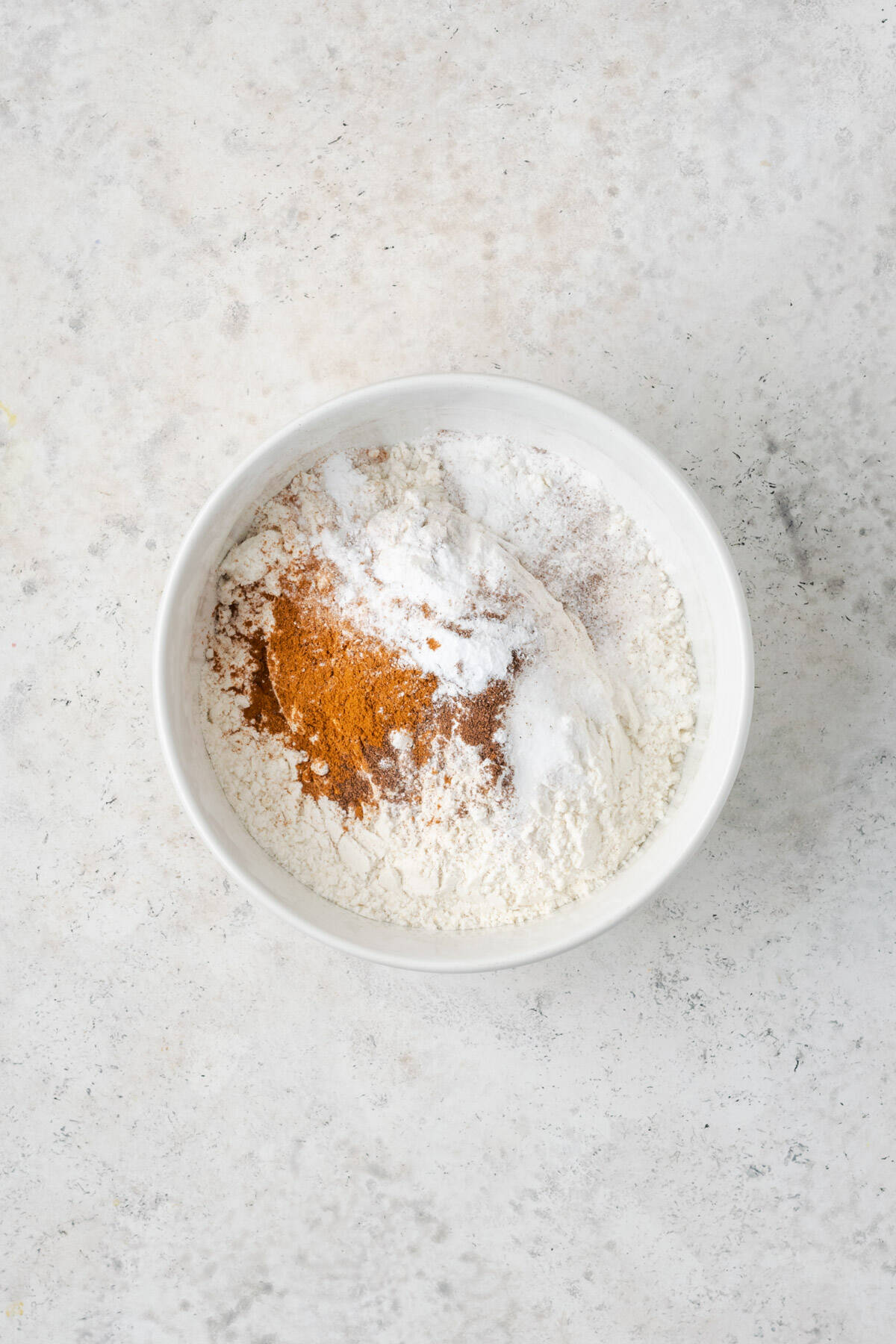 Flour, baking powder, salt, cinnamon and nutmeg in a small white bowl. 