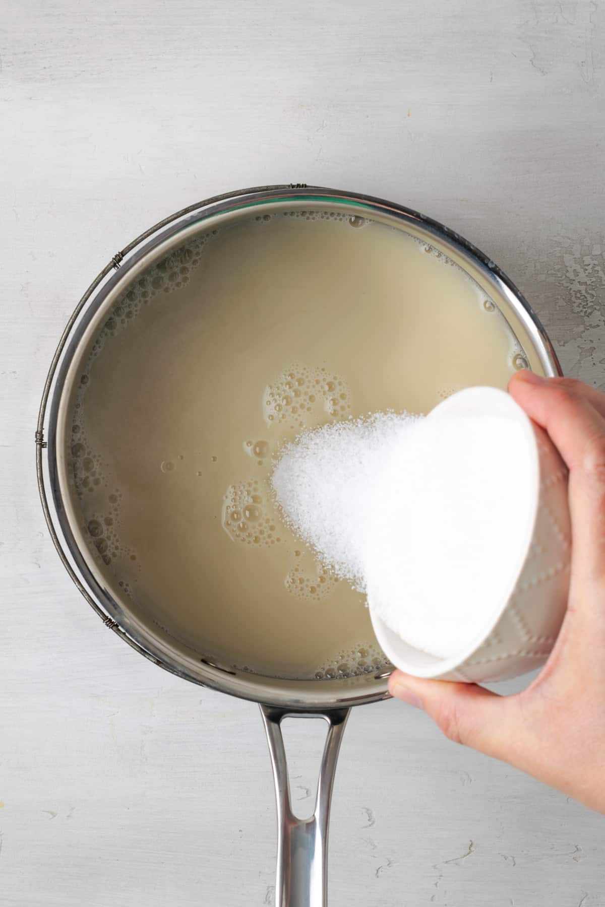 Oat milk and sugar being poured into a saucepan.