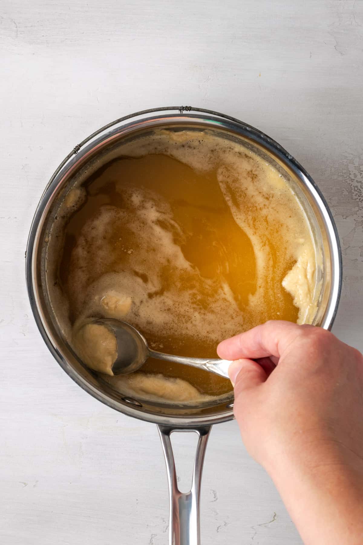 A spoon skimming the foam off of the cooked condensed milk.