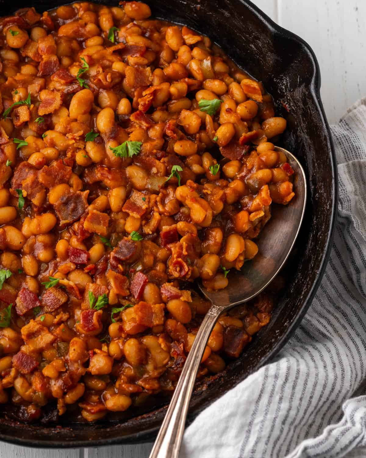 A cast iron skillet filled with bbq baked beans with pieces of bacon. 