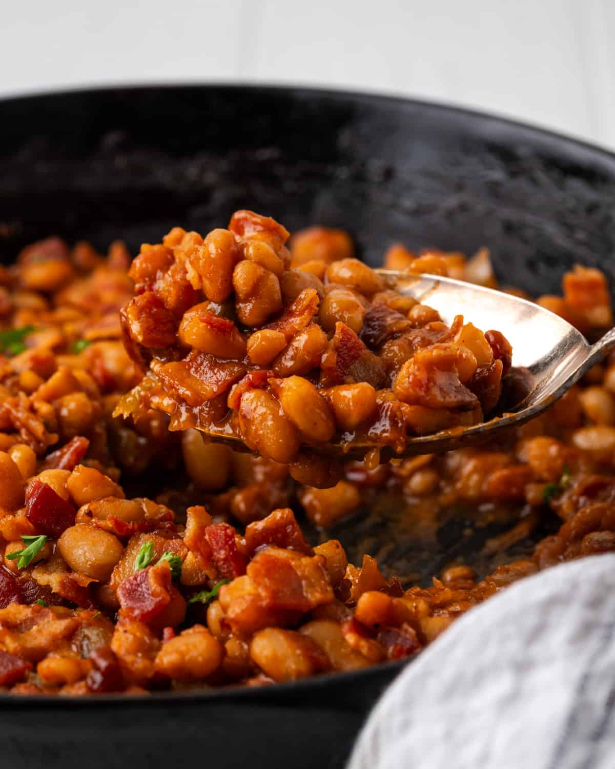 A spoon scooping out a helping of bbq baked beans with bacon.