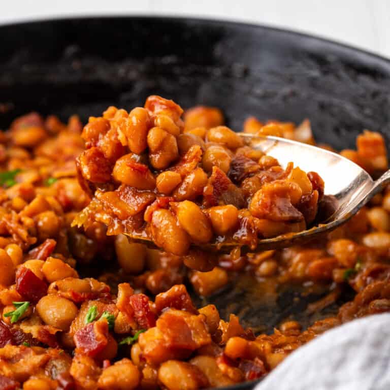 A serving spoon dishing out gluten free baked beans with bacon pieces.