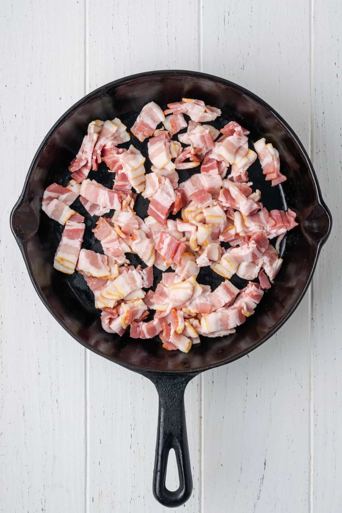 Cut pieces of bacon in a cast iron skillet.