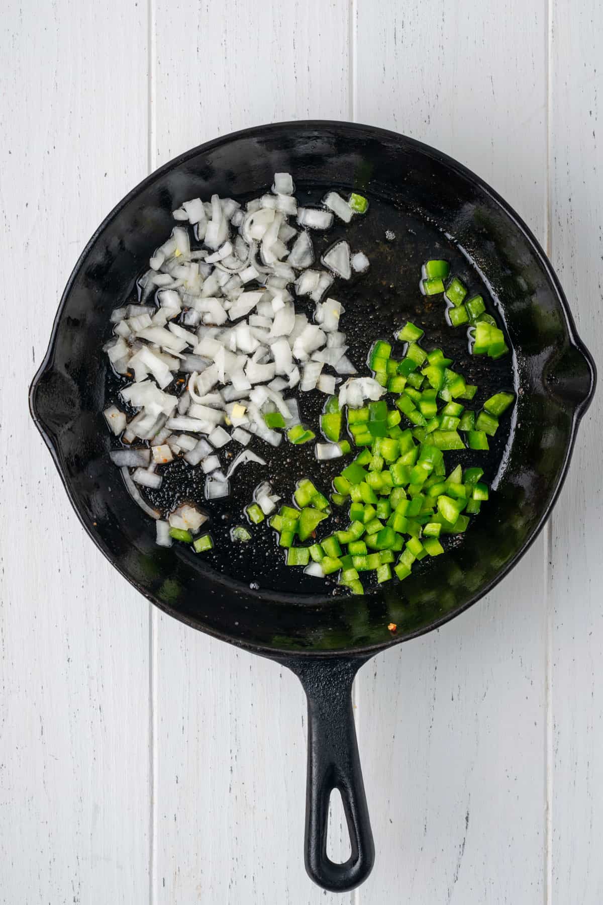 Onions and green peppers being cooked in bacon grease in a cast iron skillet.