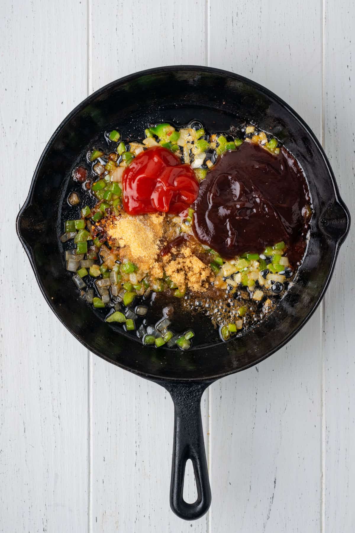 Cooked vegetables, bbq sauce, ketchup and spices in a cast iron skillet.