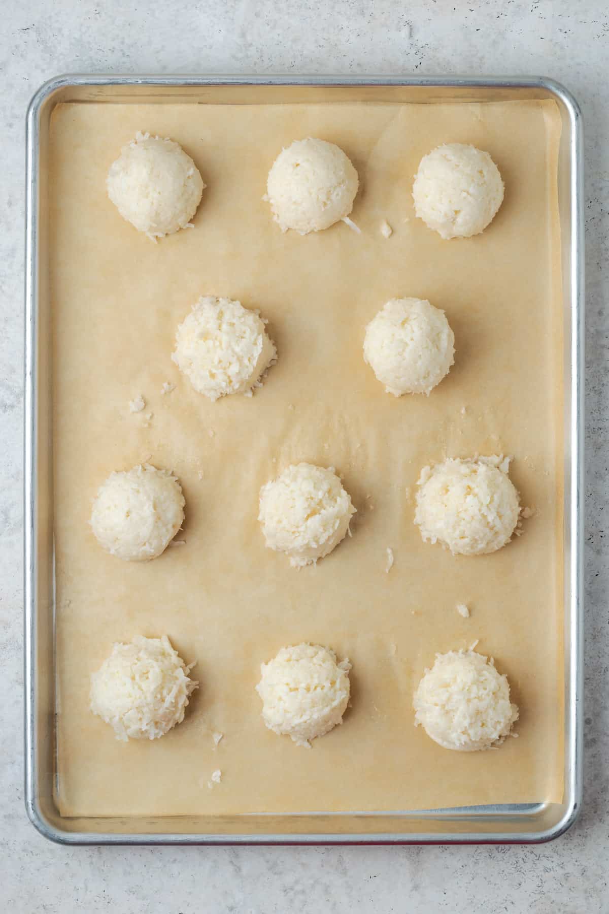 Unbaked coconut macaroons on a paper lined baking sheet. 