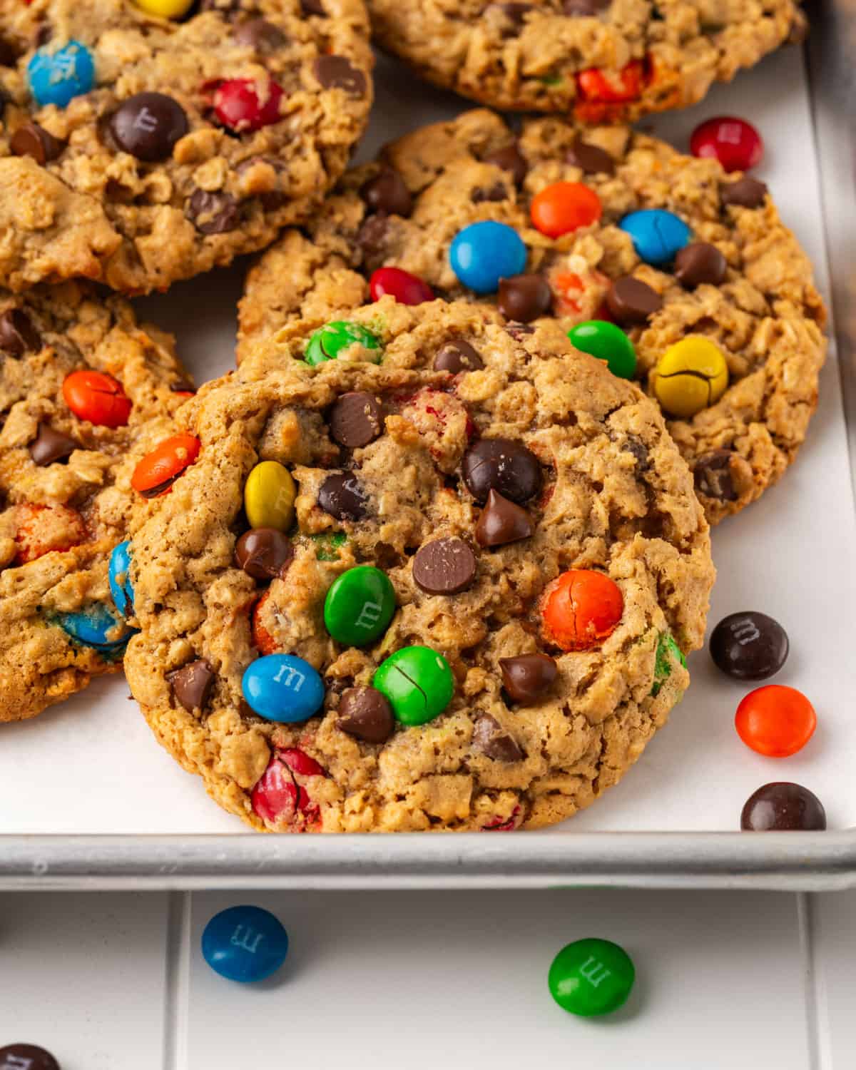 Gluten free monster cookies scattered on a metal baking sheet. 