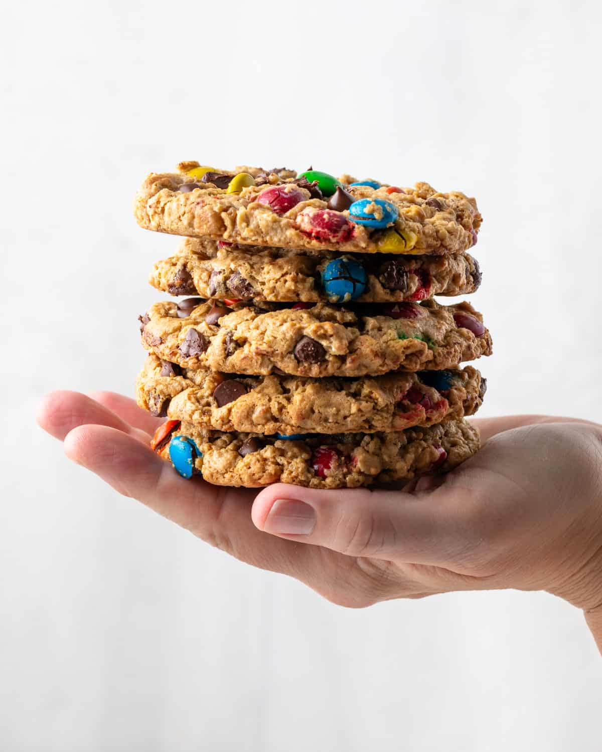 A hand holding a stack of 5 giant gluten free monster cookies. 