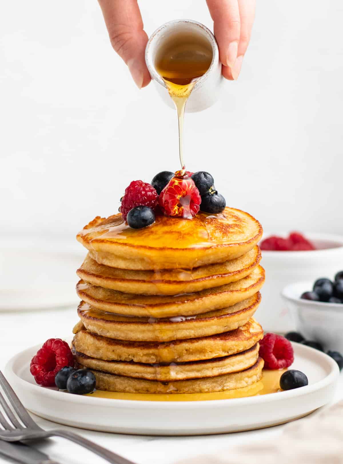 A stack of grain free pancakes topped with maple syrup and fresh berries on a white plate.