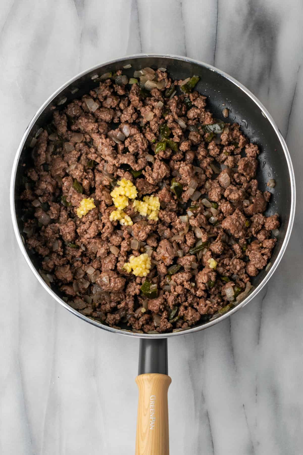 Minced garlic being added to cooked ground beef. 