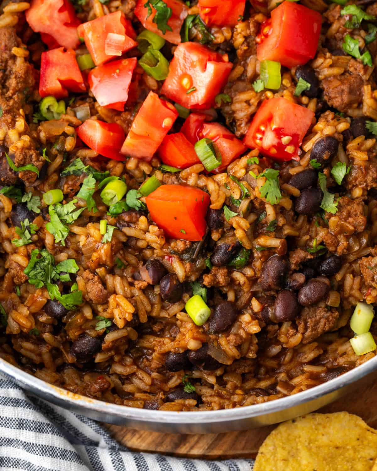 Mexican beef and rice in a skillet topped with tomatoes, cilantro and green onions.