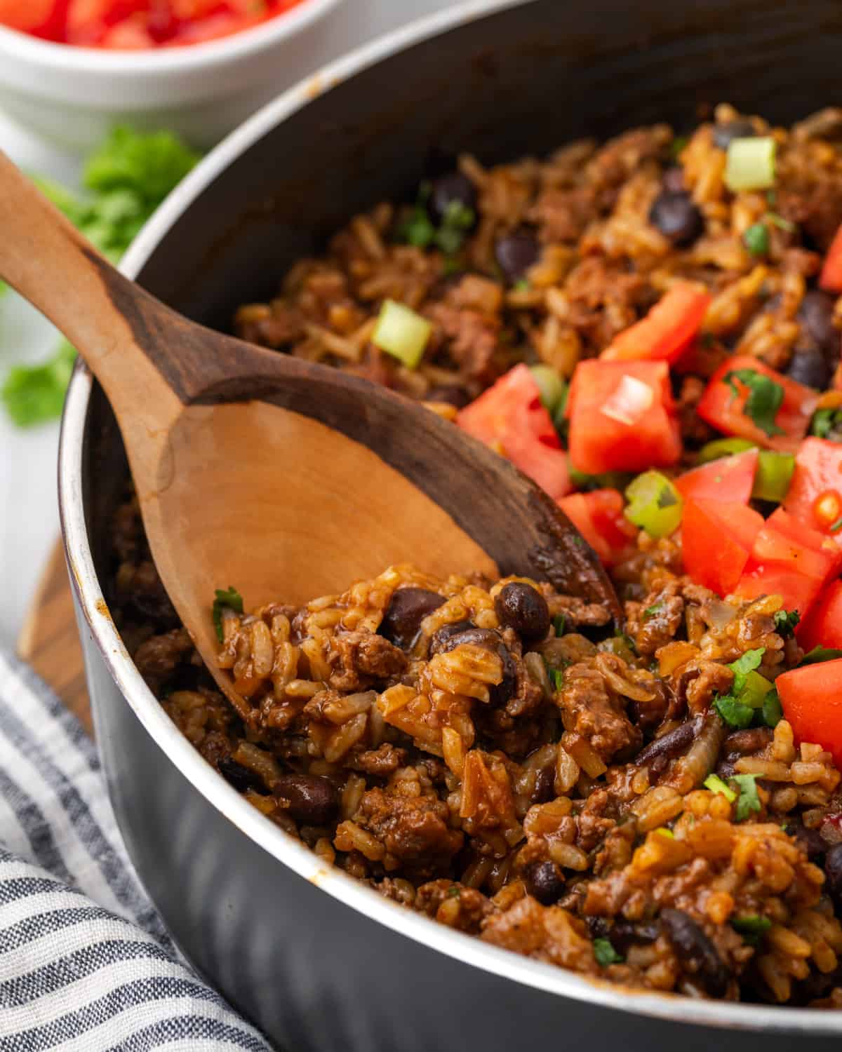 A wooden spoon scooping Mexican beef and rice out of the skillet.